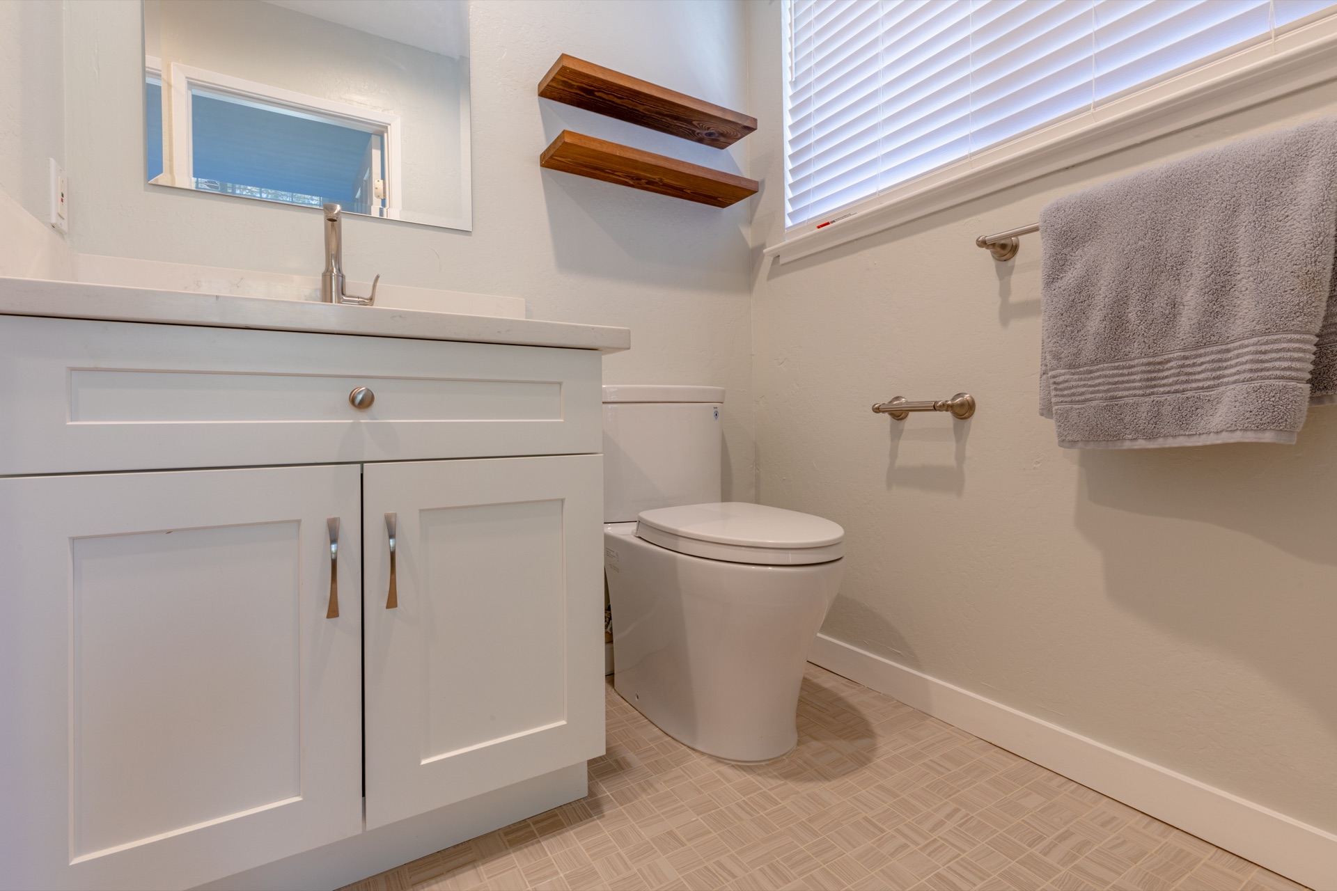 Small white bathroom with shaker vanity, floating wood shelves, and herringbone floor tile