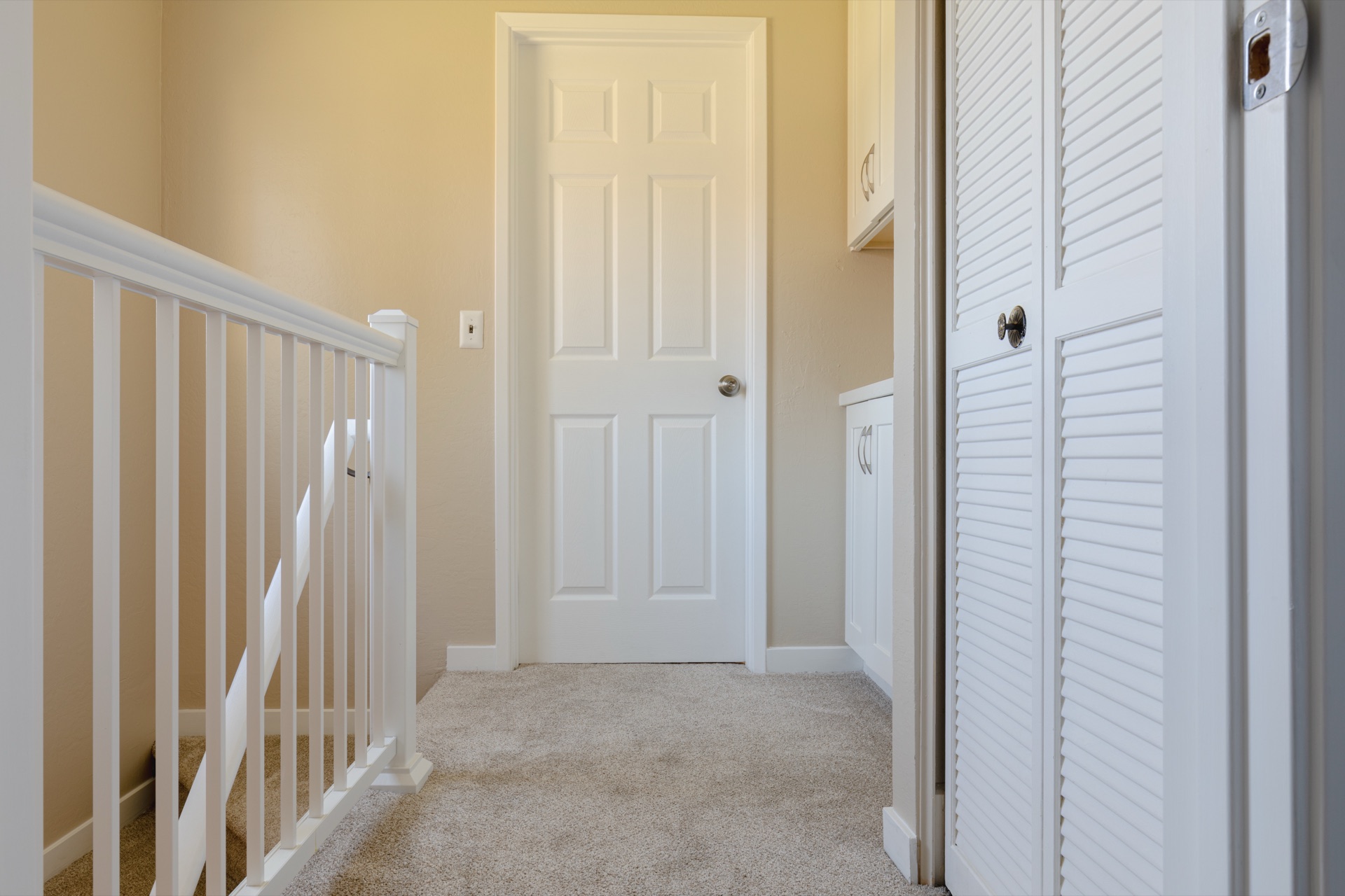 Upstairs landing with white railing, louvered closet doors, and neutral carpet