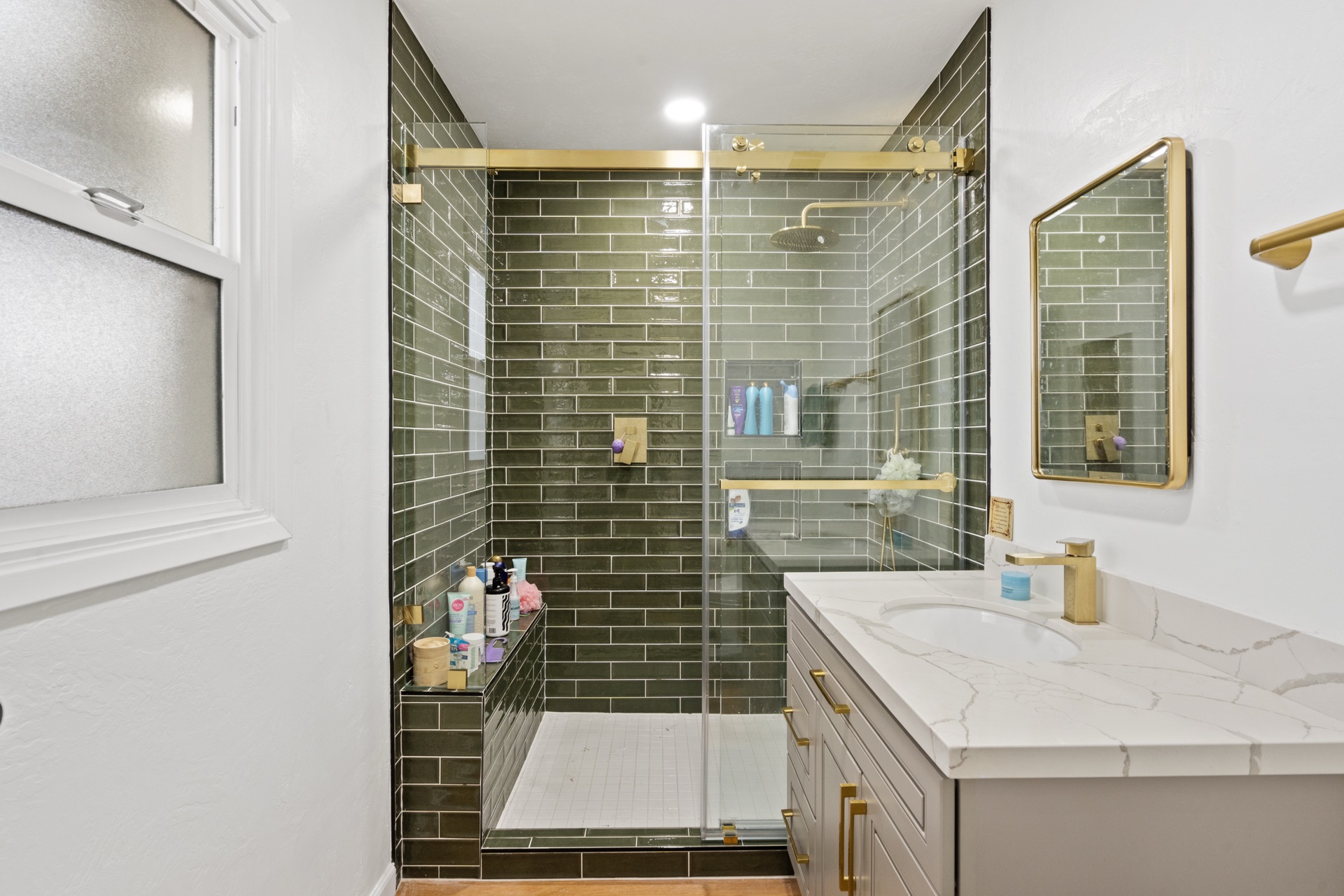 Bathroom with green subway tile shower, gold shower head, and marble-look floating vanity