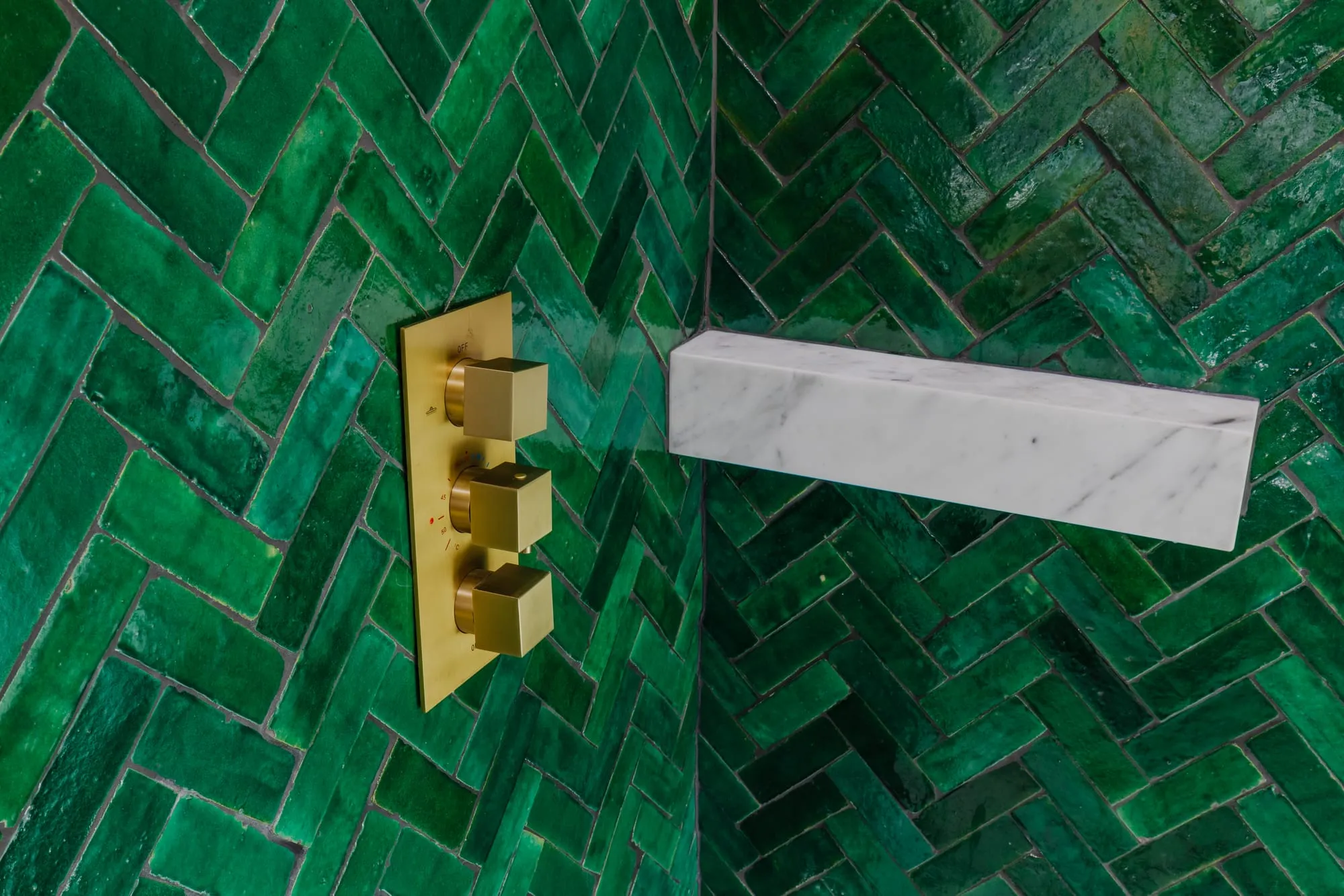Brass shower valve and a solid marble shelf set into the emerald herringbone tile
