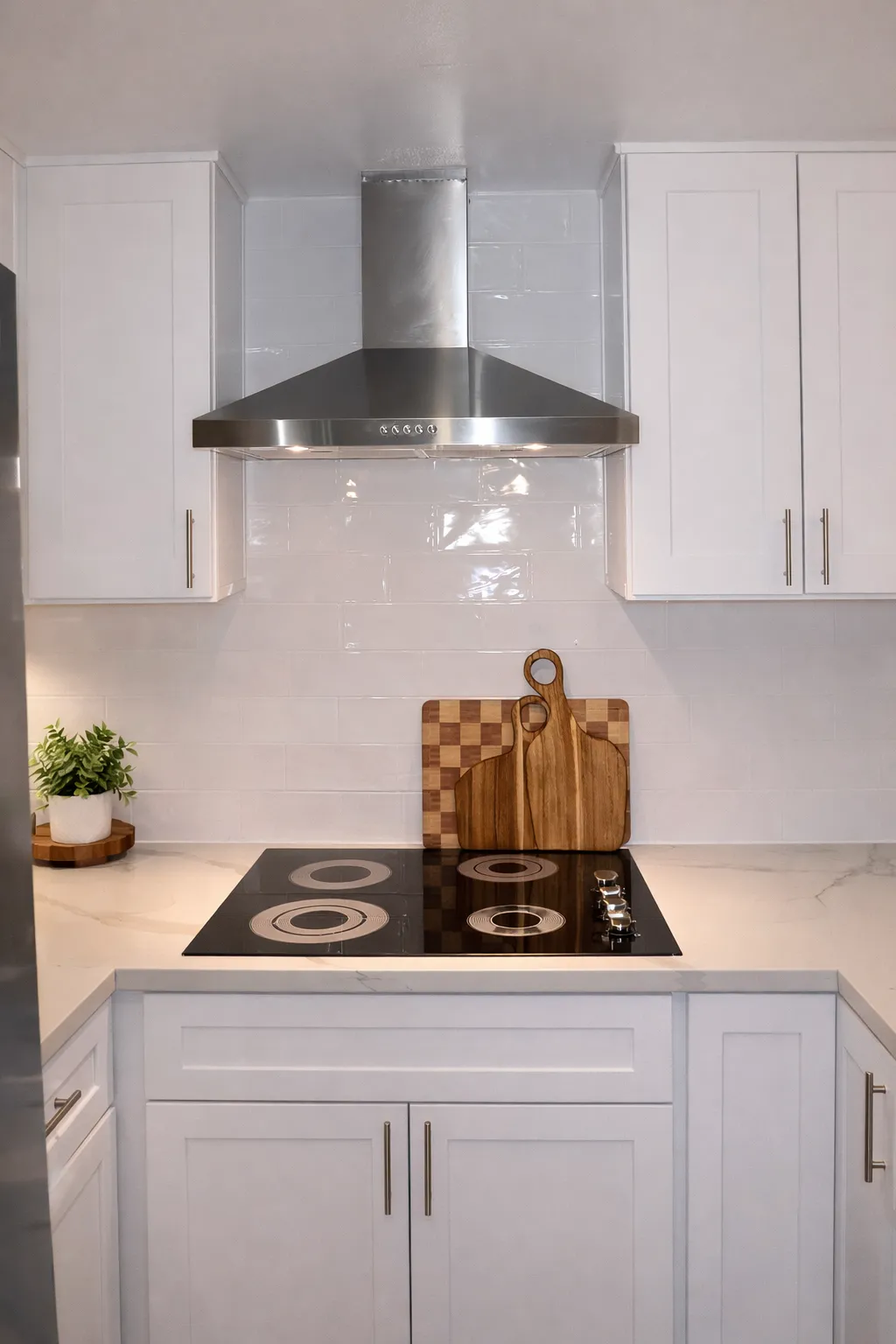 Stainless chimney hood above the black glass cooktop against a white subway tile wall with thin grout
