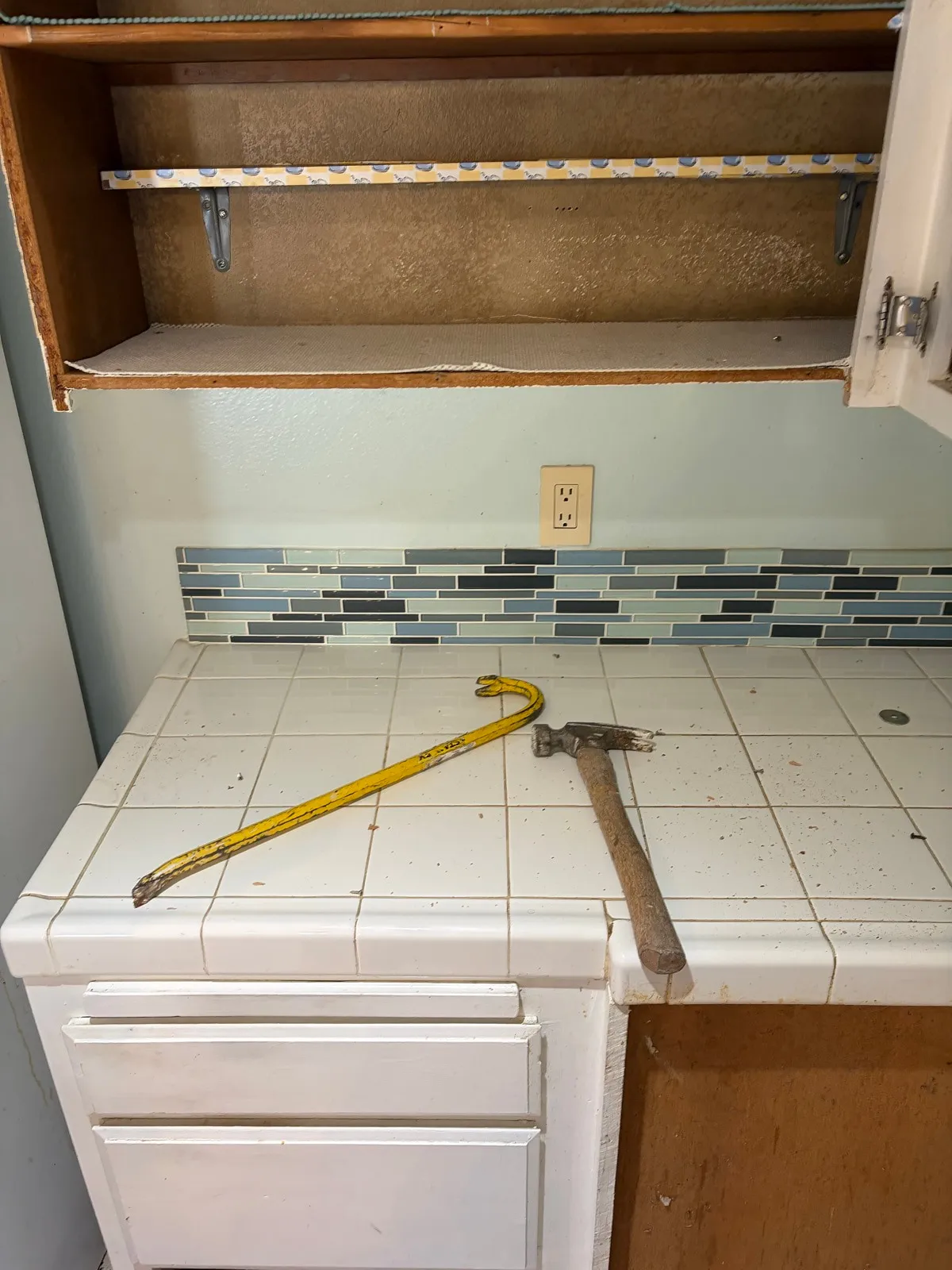 Kitchen during demolition, hammer and pry bar resting on the stripped subfloor