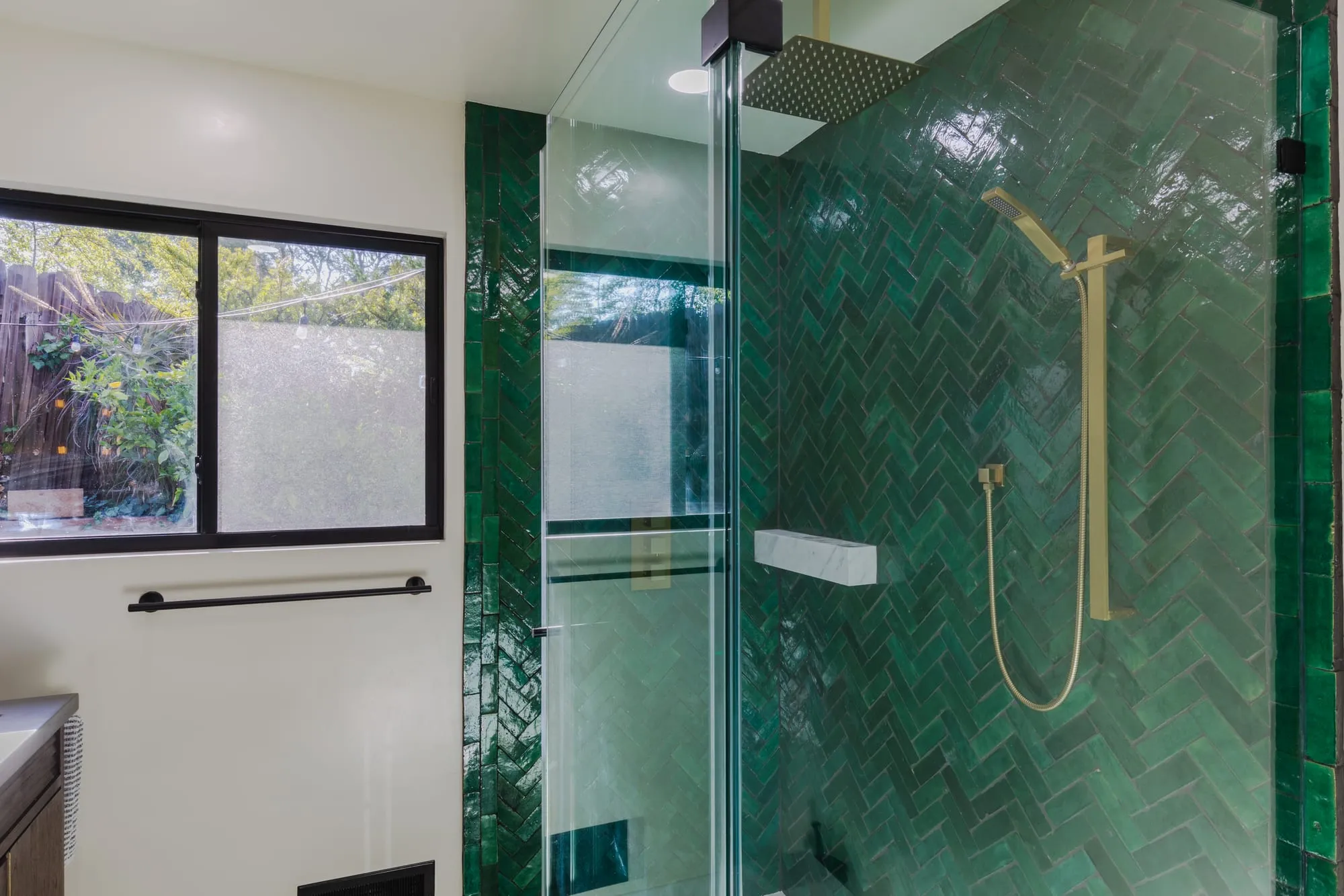 Emerald herringbone tile lining the shower with a brass rain head and hand shower