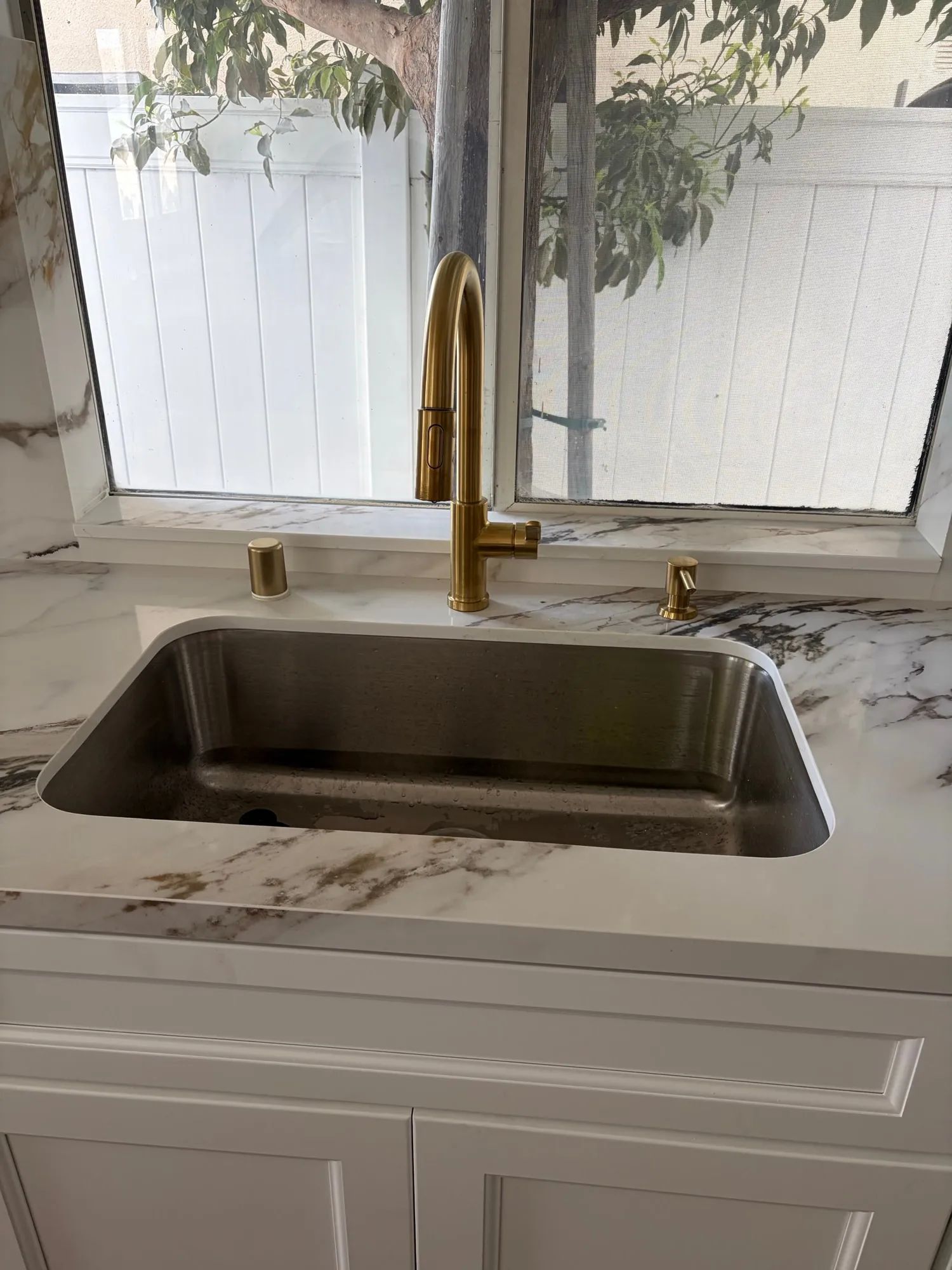 Brushed-gold faucet against the marble-look slab backsplash