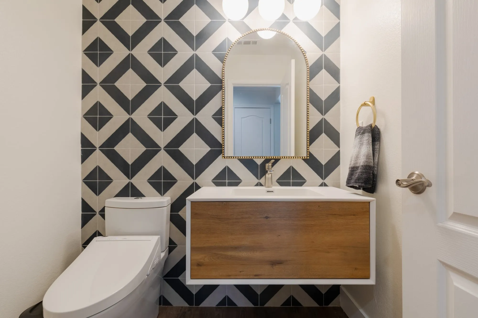 Bathroom after remodel, black and white geometric tile wall behind a floating oak vanity