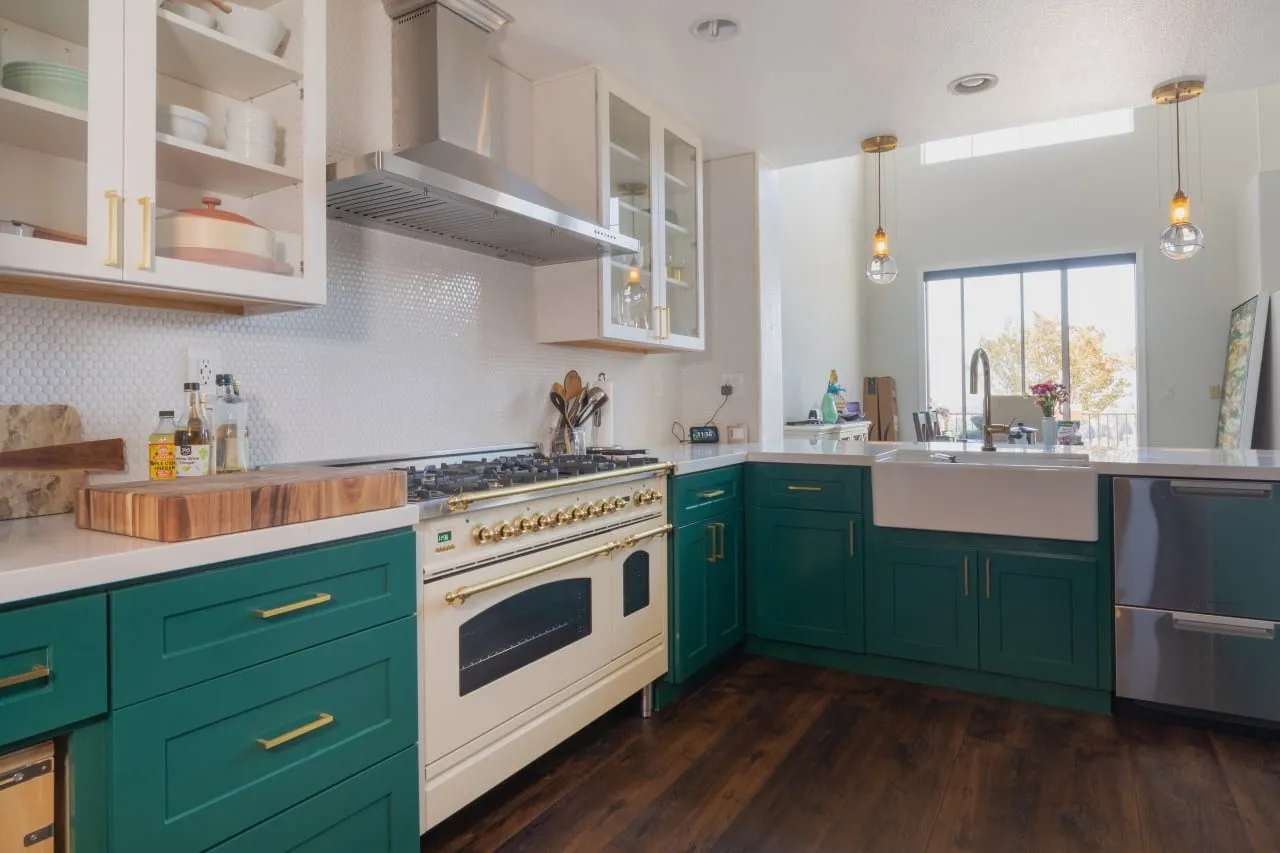 Kitchen after remodel, emerald shaker cabinetry with brass hardware around a cream range and an apron sink