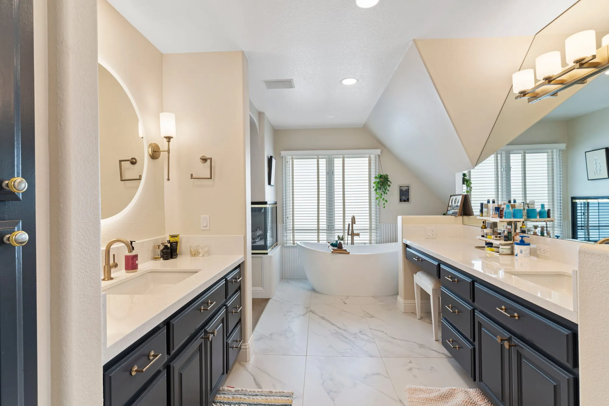 Bathroom after remodel, navy shaker vanity run with brass fittings under a vaulted ceiling