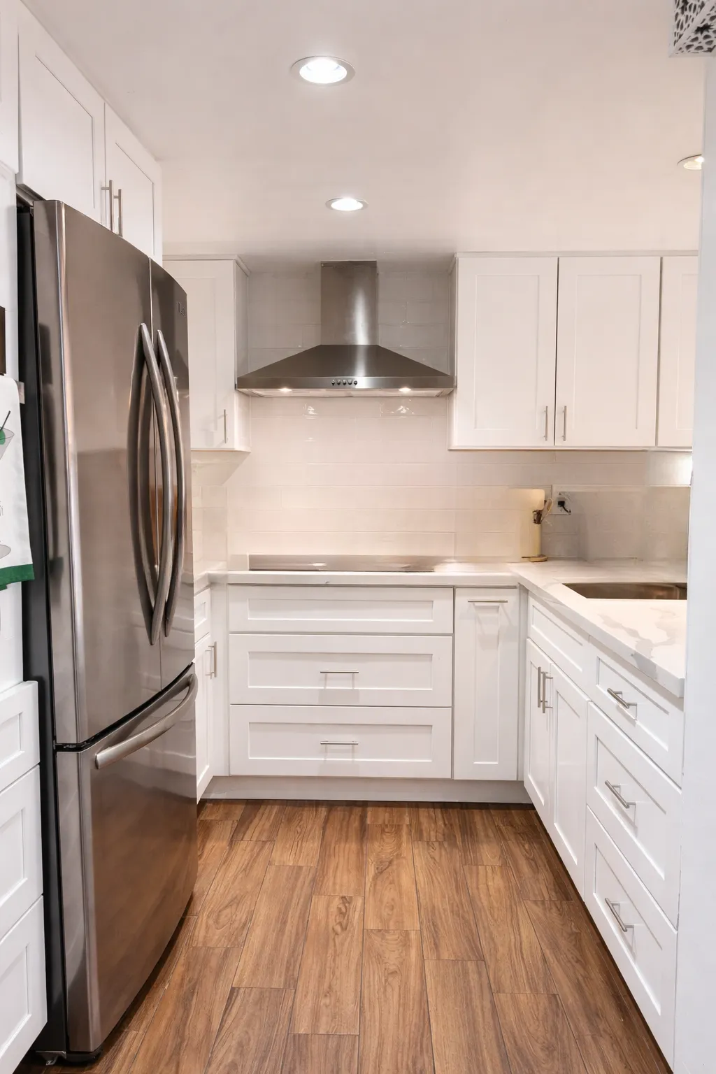 U-shape kitchen after remodel, white shaker cabinetry with light quartz counters and a peninsula