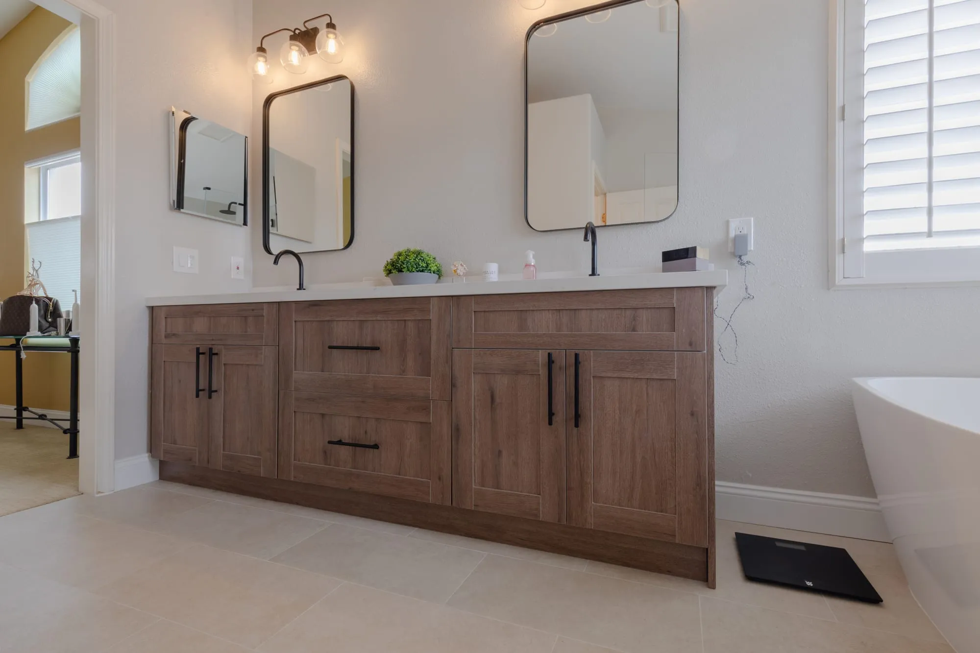 Bathroom after remodel, wood shaker double vanity under twin black-framed mirrors beside a freestanding tub