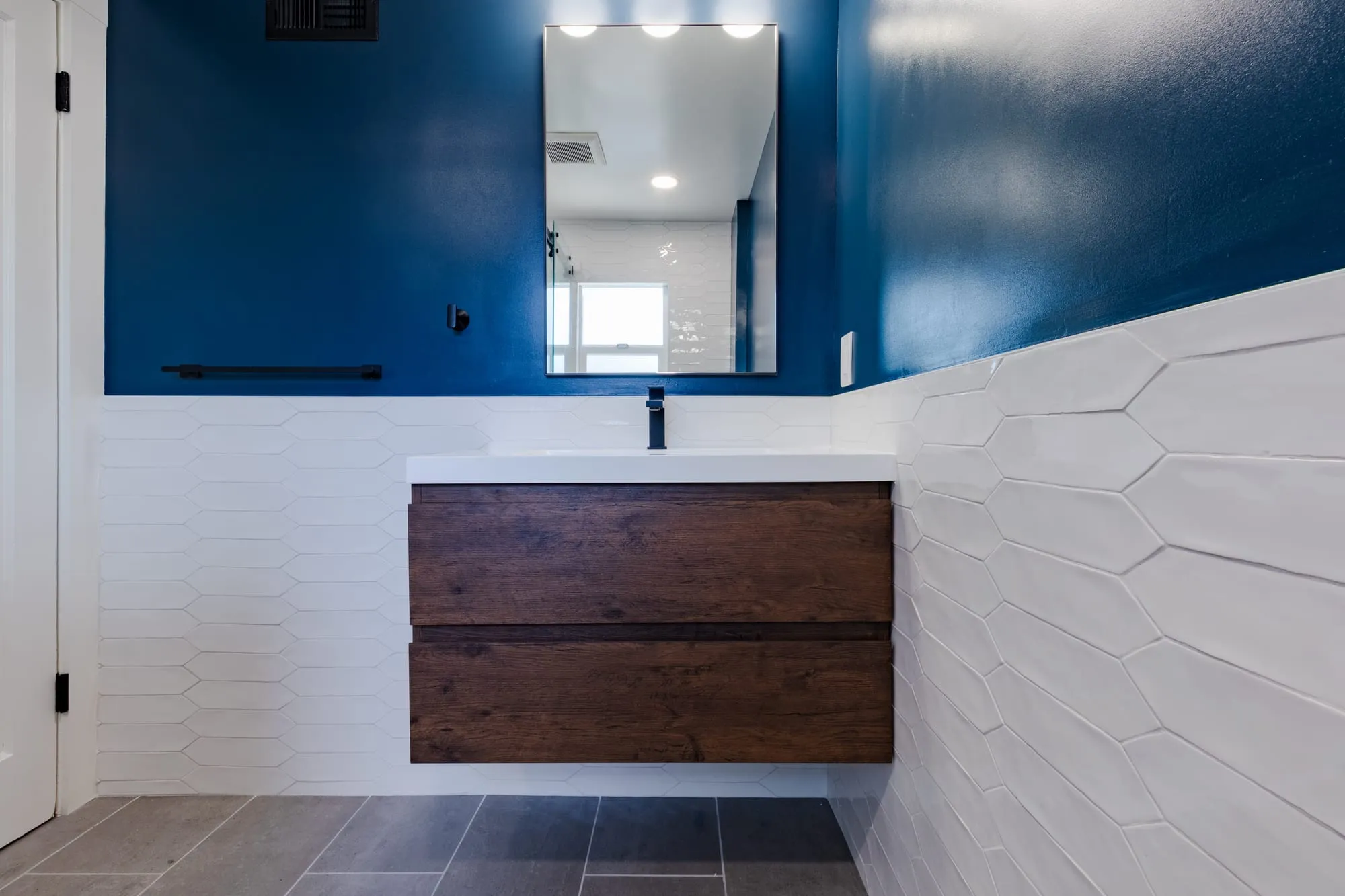 Bathroom after remodel, floating walnut vanity below a deep navy wall with textured white tile