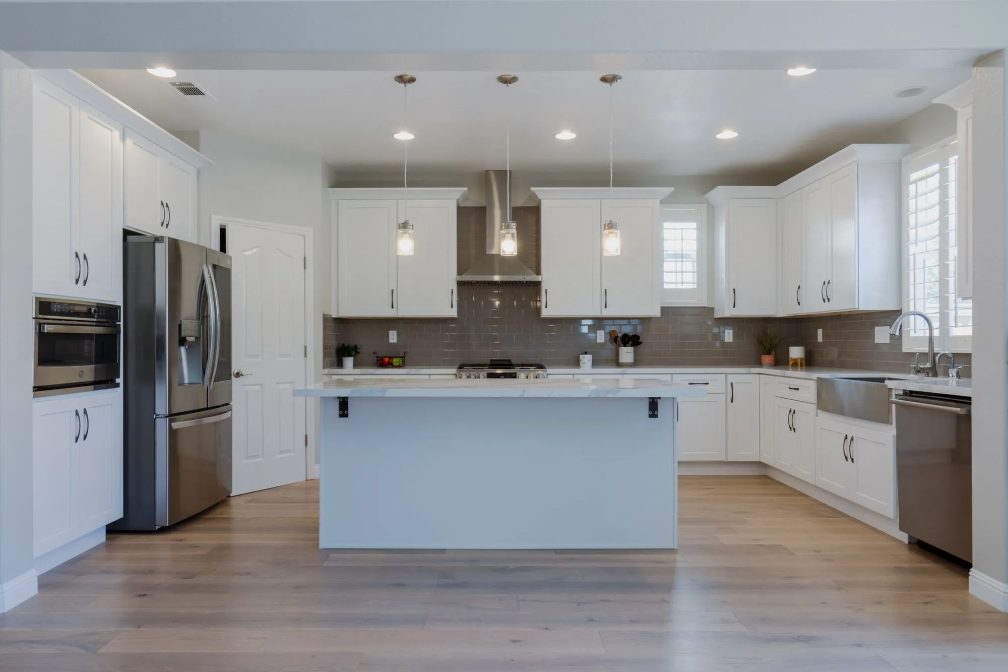 White shaker kitchen after remodel, marble-look quartz island below glass pendants