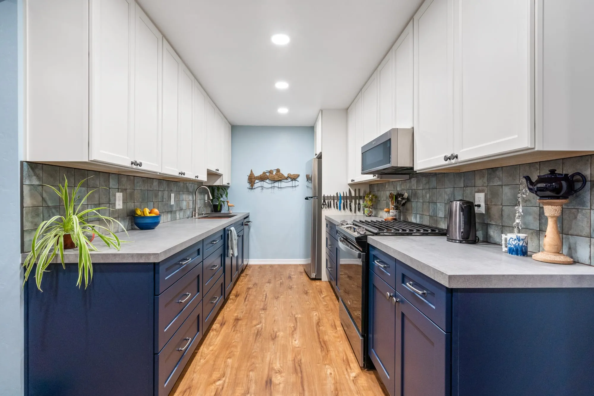 Kitchen after remodel, navy shaker lowers under white uppers with a slate-tone tile backsplash