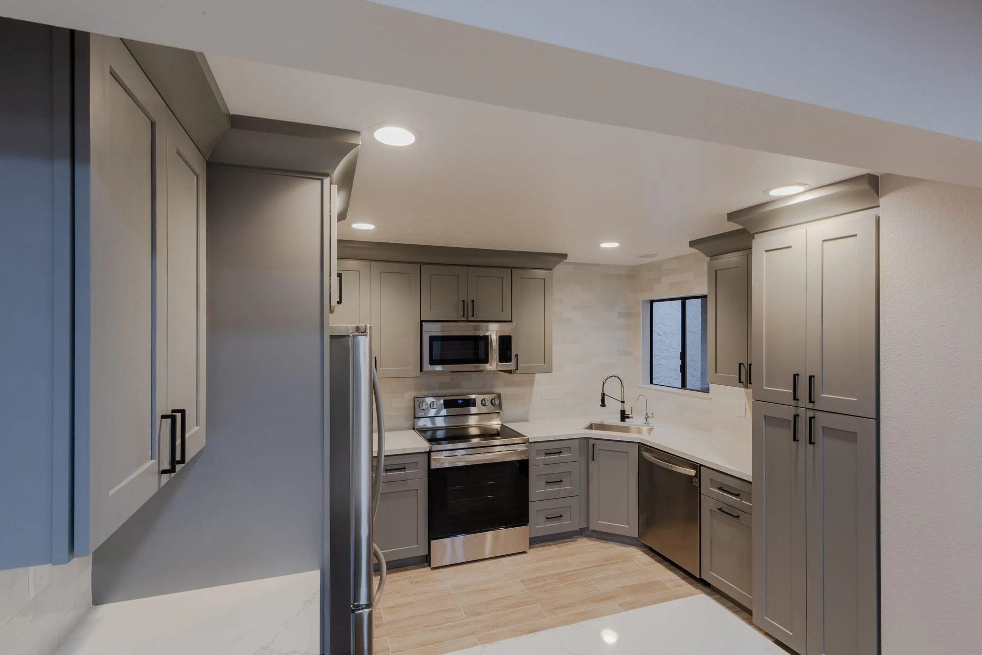 Kitchen after remodel, warm grey shaker cabinetry with quartz counters and stainless appliances
