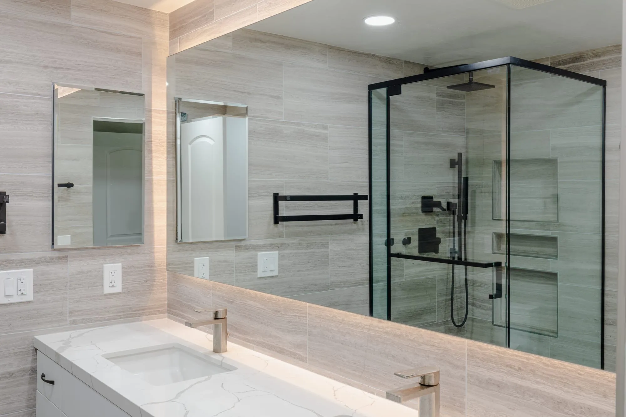Bathroom after remodel, double vanity under a backlit mirror with stone-look tile walls and a glass shower
