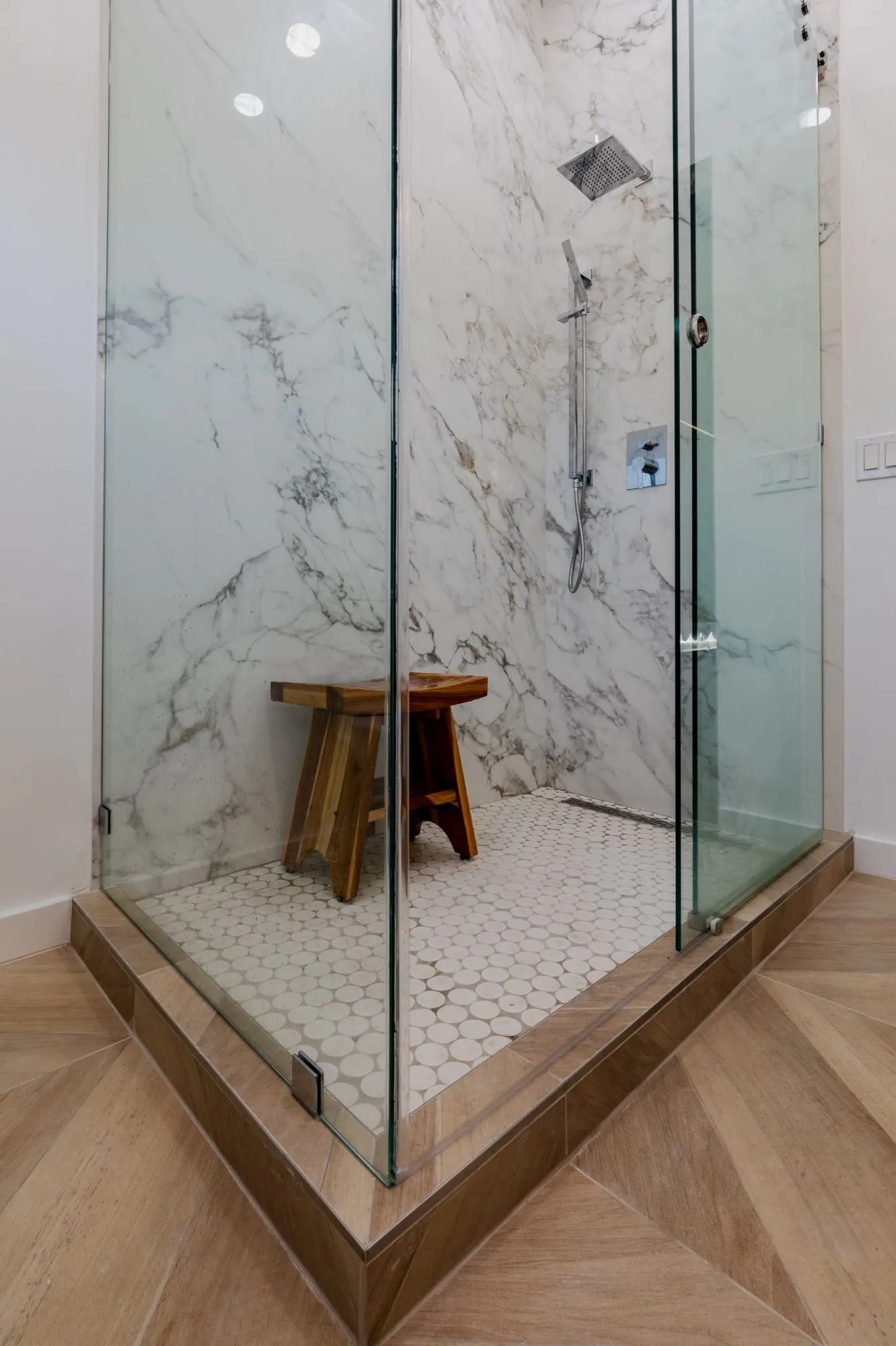 Frameless glass shower after remodel, marble-veined slab walls with white hex tile floor