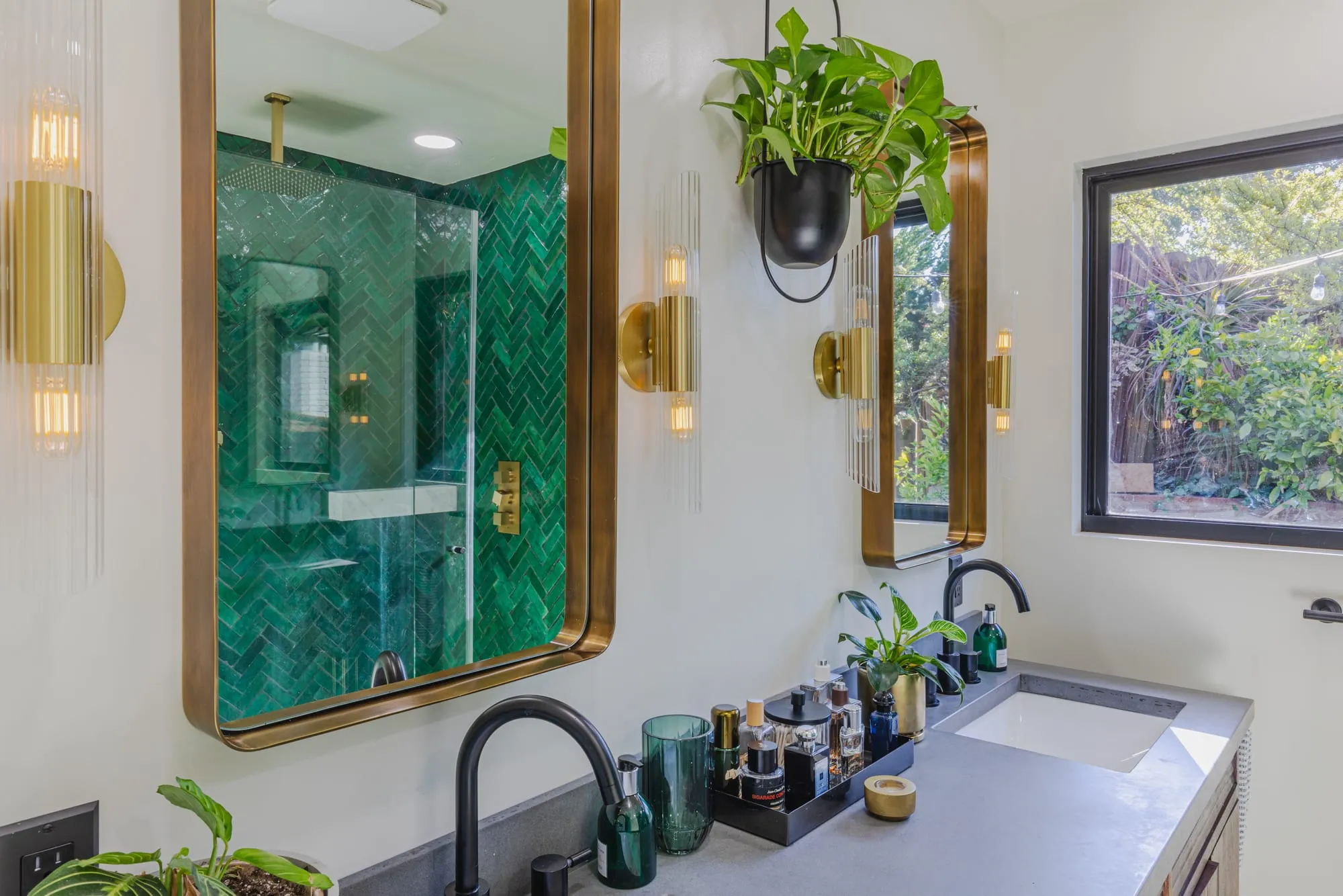 Bathroom after remodel, emerald herringbone tile shower behind glass with brass-framed mirrors over a double vanity