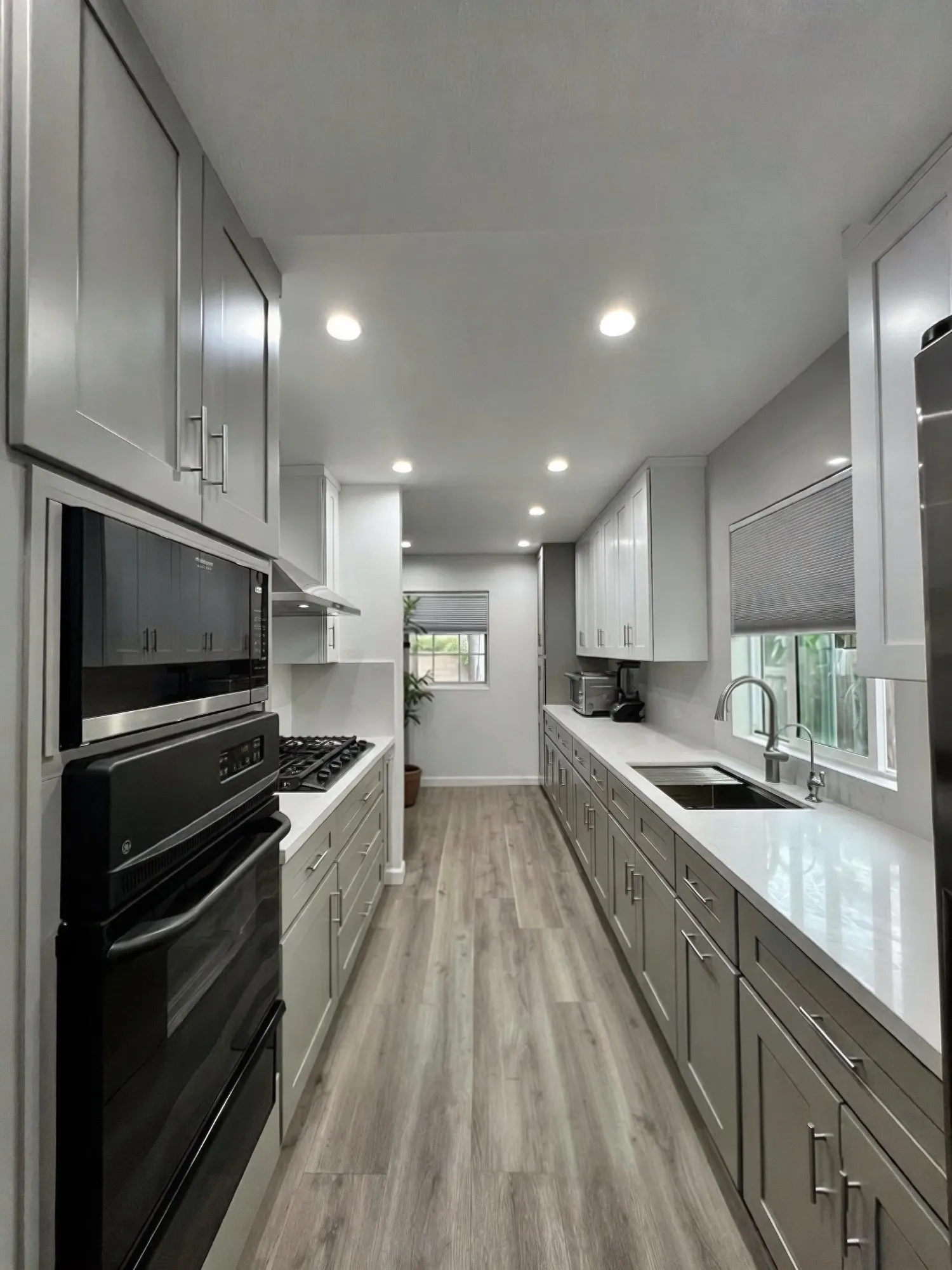 Galley kitchen after remodel, white uppers over warm grey shaker lowers with white quartz counters