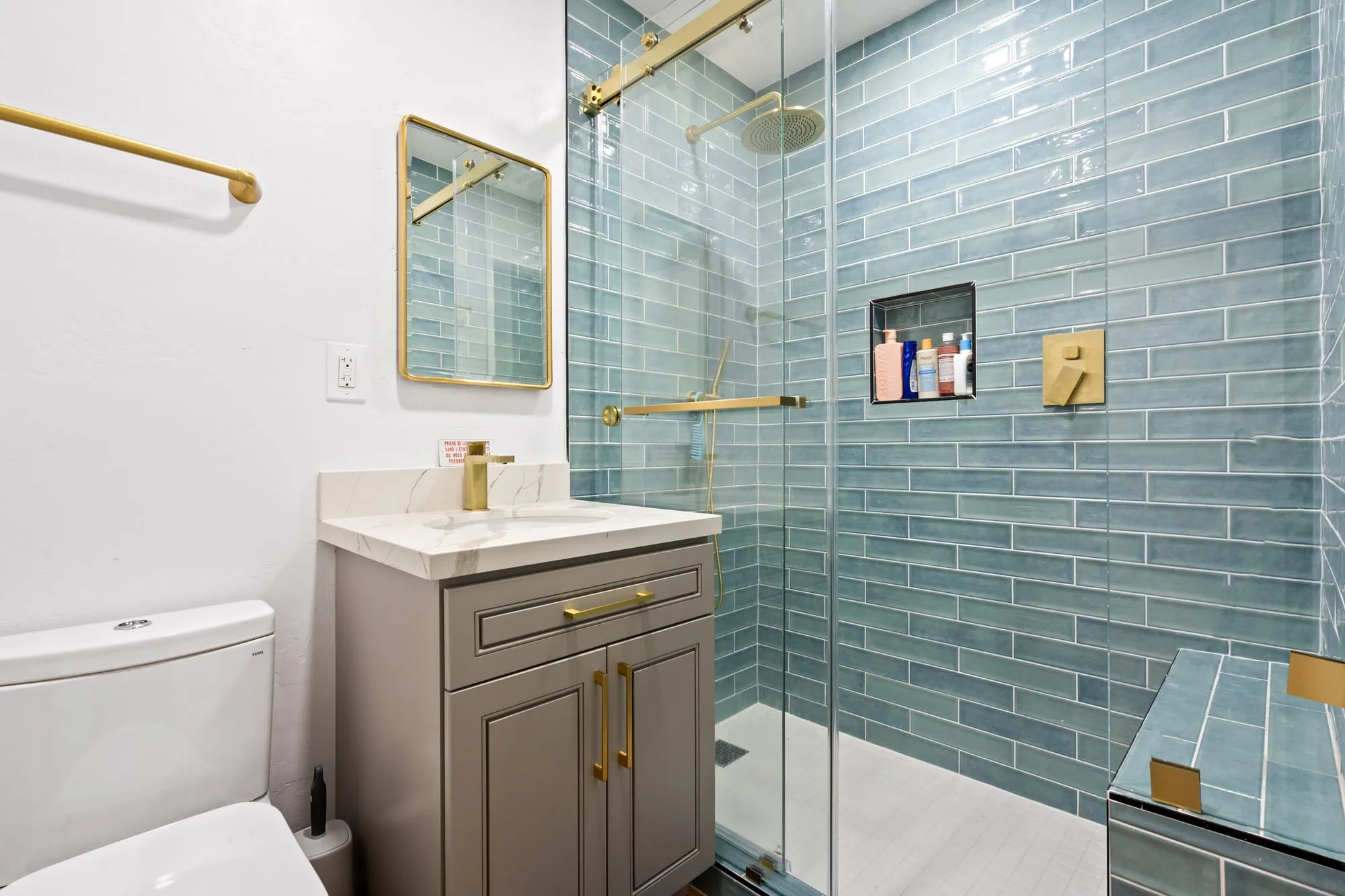 Bathroom after remodel, aqua glazed tile shower behind glass beside a taupe shaker vanity