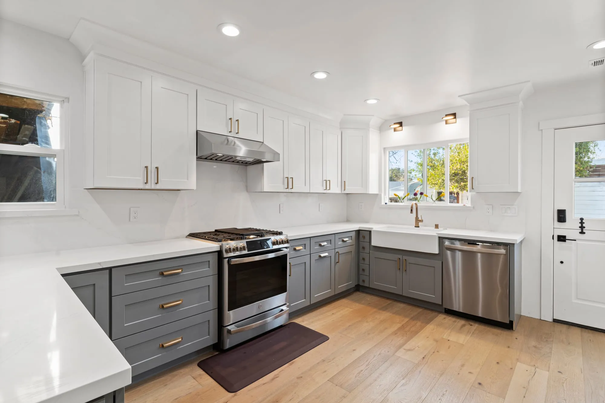 Kitchen after remodel, white uppers over grey shaker lowers with a quartz peninsula and an apron sink