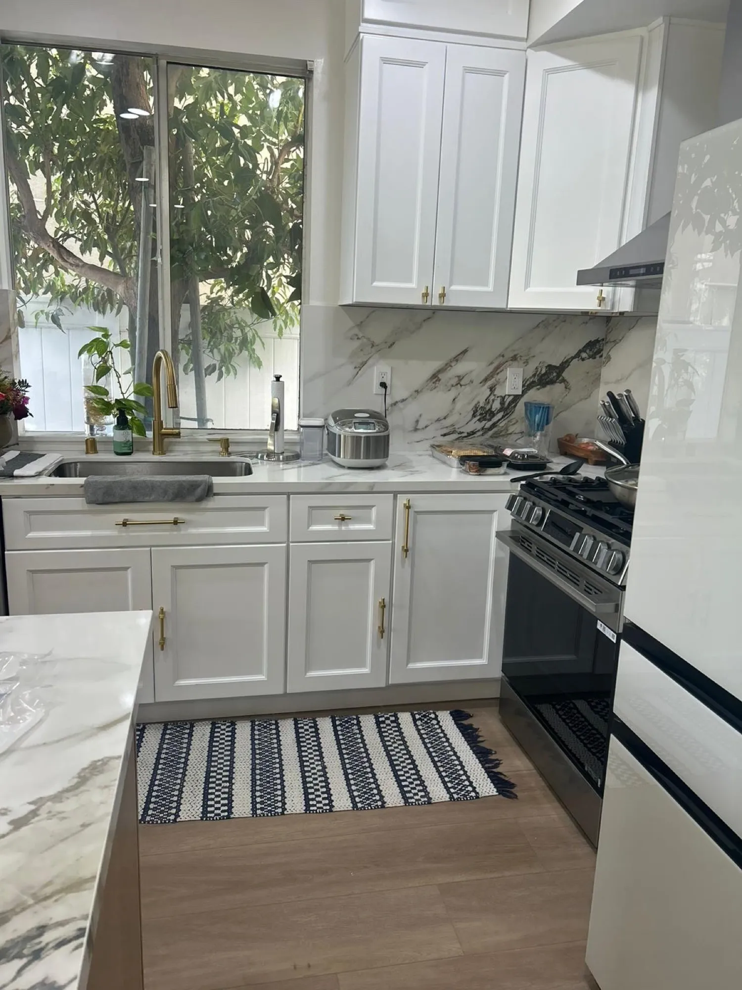 Kitchen after remodel, white cabinetry with brushed-gold hardware and a marble-look slab backsplash