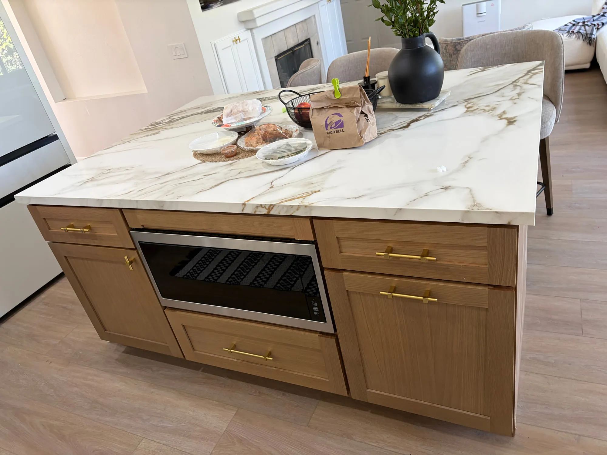 White-oak island with a marble-look waterfall top and a microwave drawer, open to the living room beyond