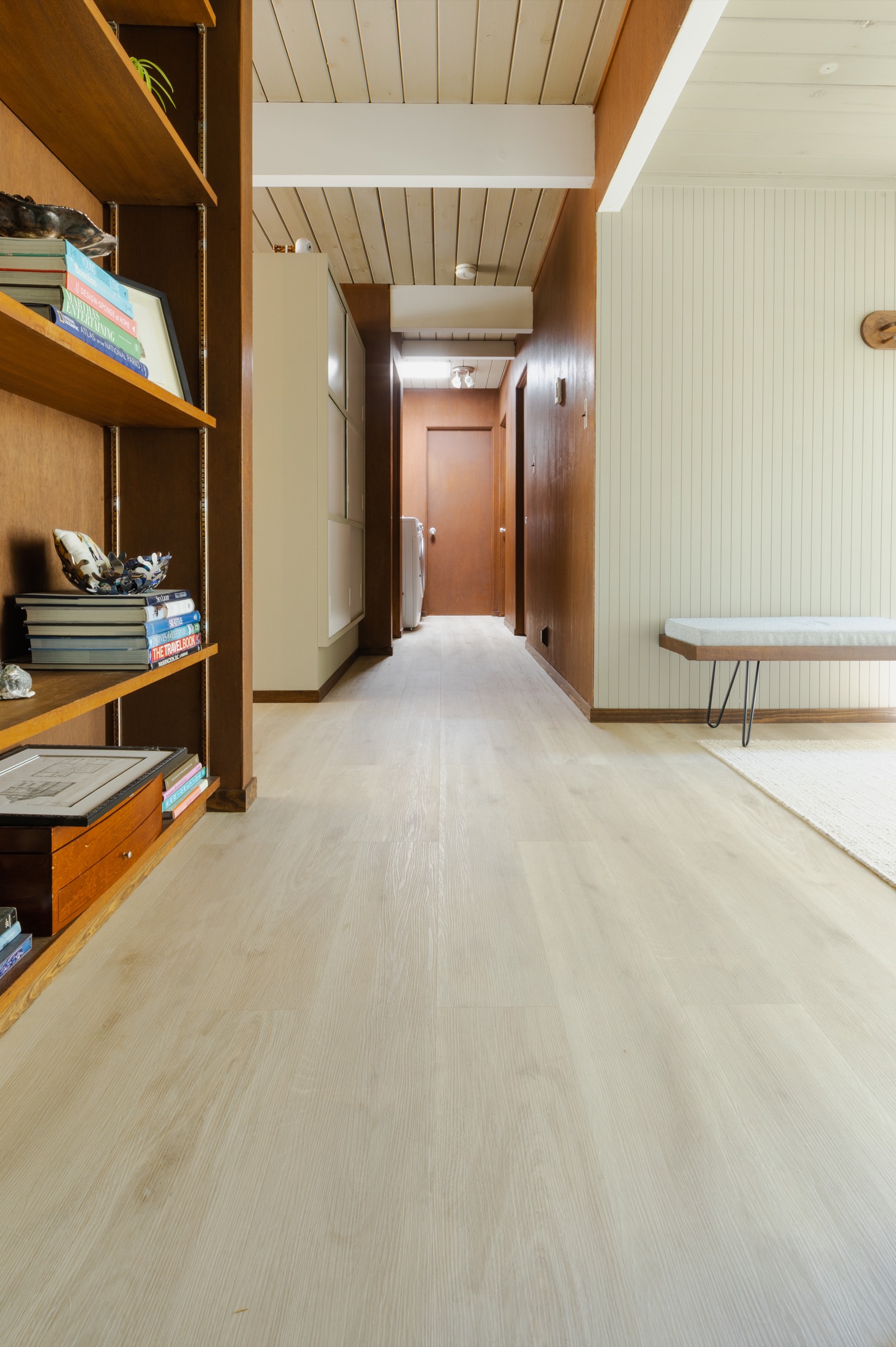 Mid-century modern entry hallway with warm wood shelving, tongue-and-groove ceiling, and light oak floor