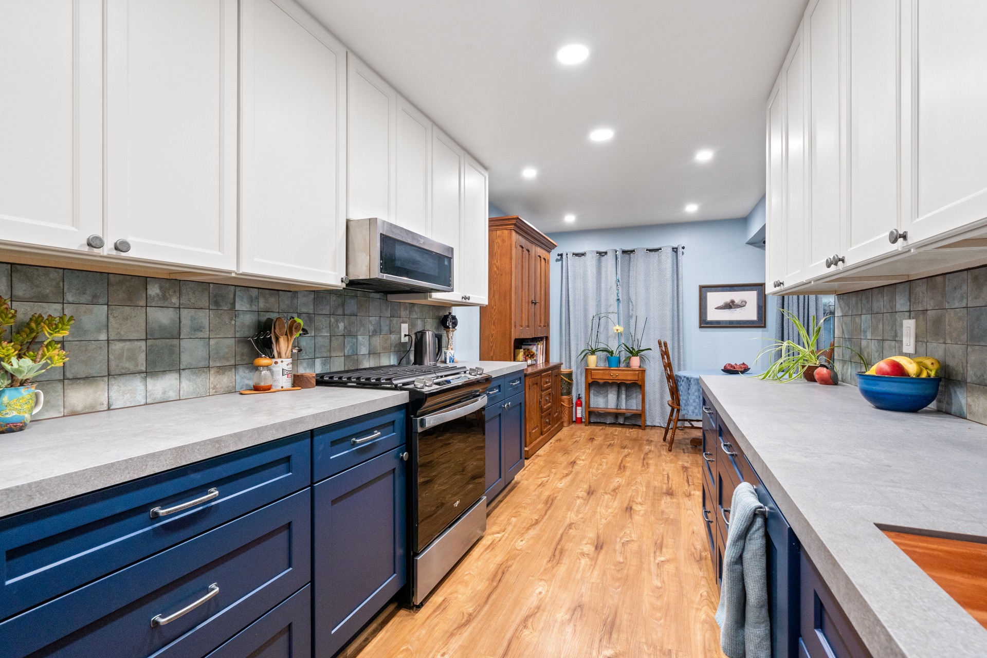 Navy blue kitchen with gray tile backsplash, stainless range, and open flow to dining