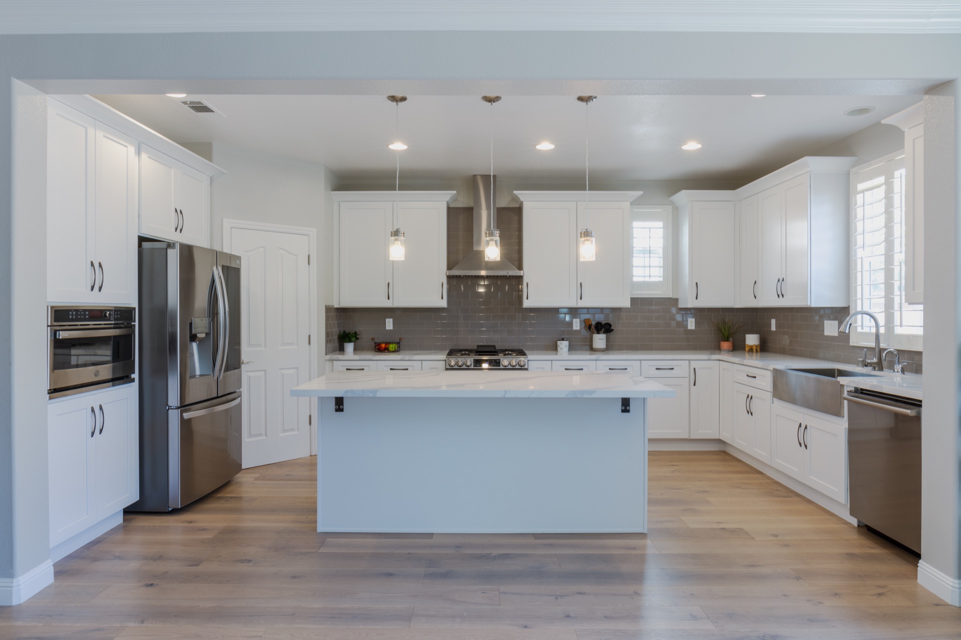 White shaker kitchen with center island, gray subway tile backsplash, pendant lights, and stainless appliances