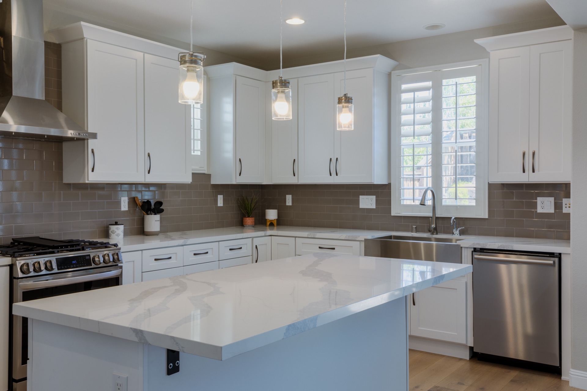 White shaker kitchen — marble island, gas range, and glass pendant lighting
