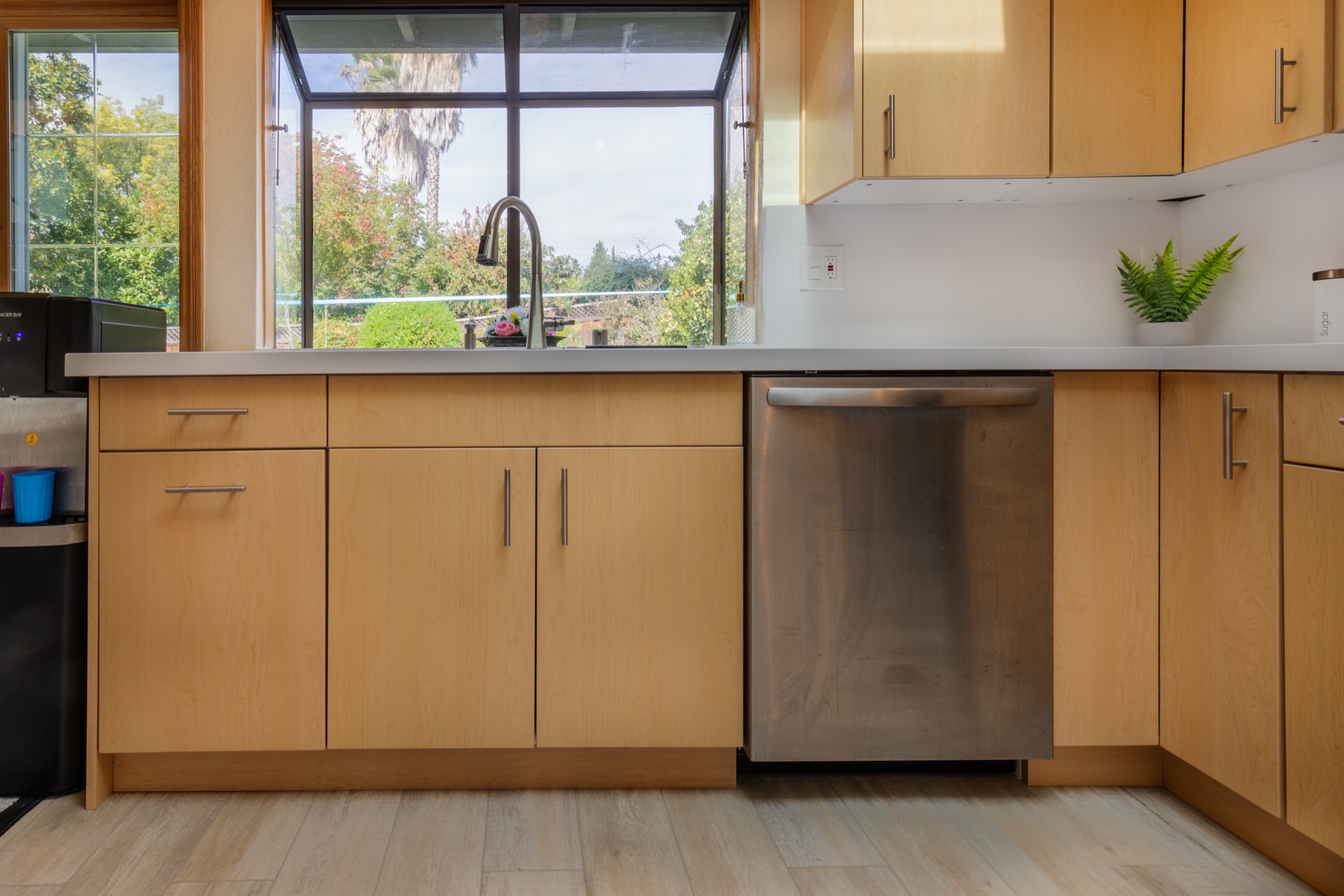 Warm-wood kitchen with large window over sink, quartz counters, and stainless dishwasher