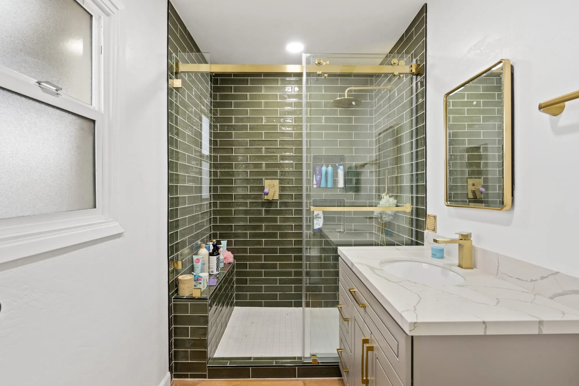 Olive glazed tile shower behind glass beside the vanity