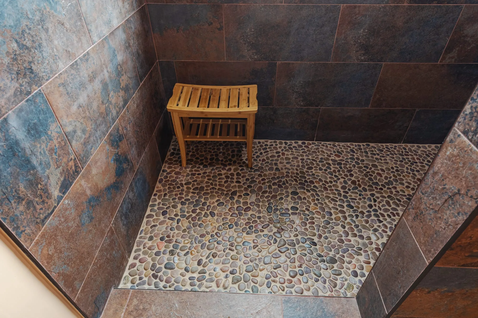Walk-in shower lined in slate-tone tile over a pebble mosaic floor
