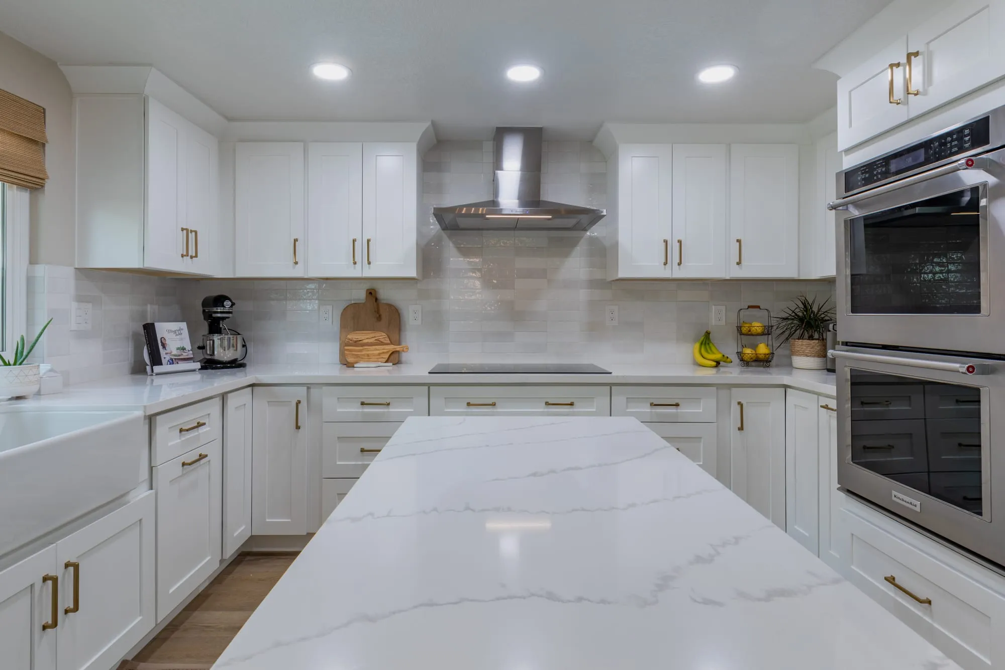 Veined quartz counter running past the cooktop to a stacked pair of wall ovens