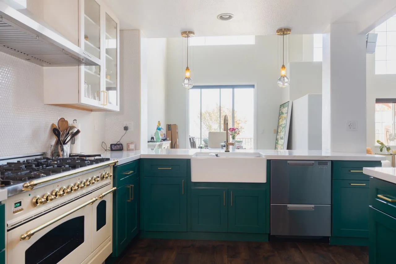 Emerald lower cabinetry running from the cream range to a white apron sink under the window