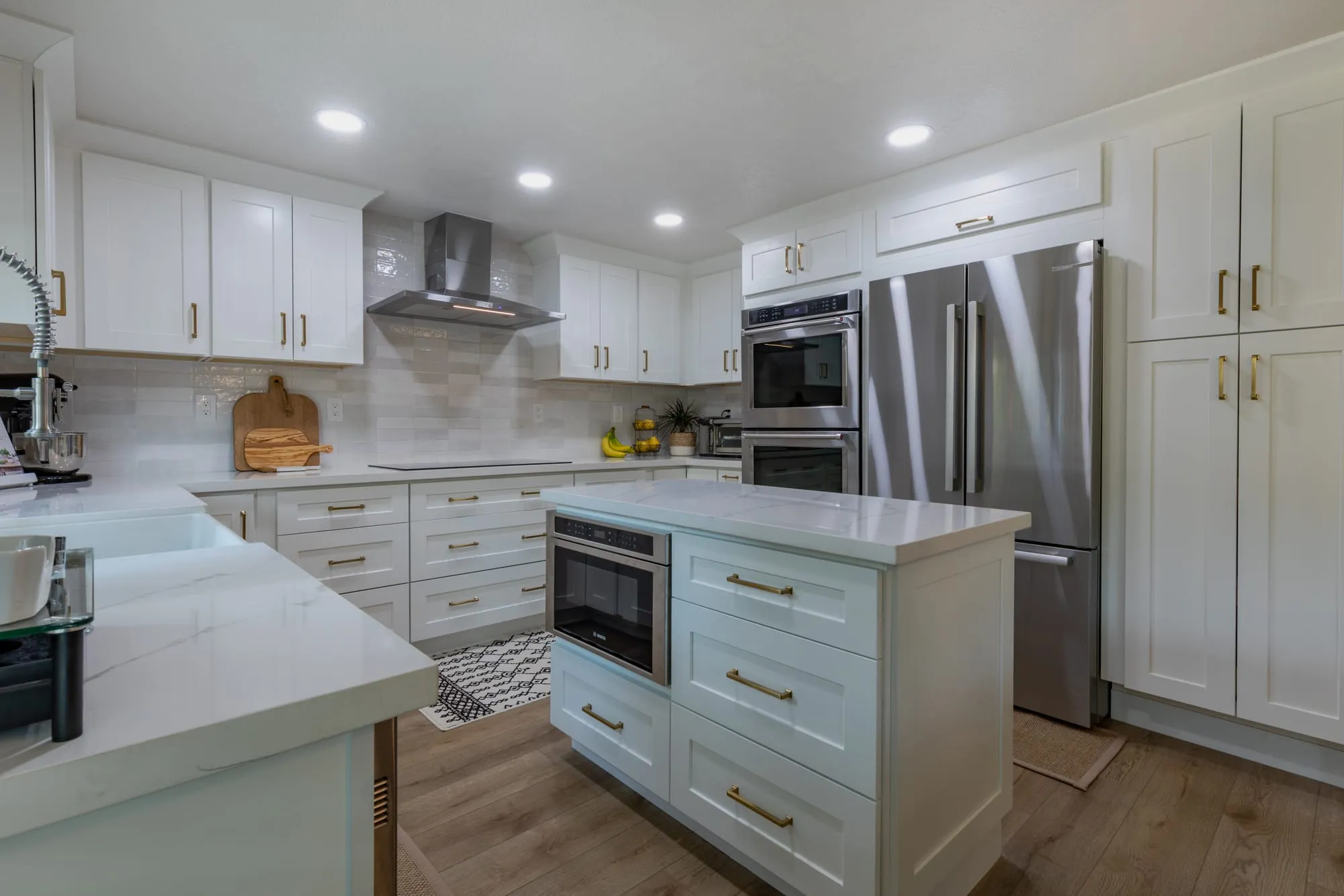 Sage-green island with brass pulls facing the wall ovens and refrigerator