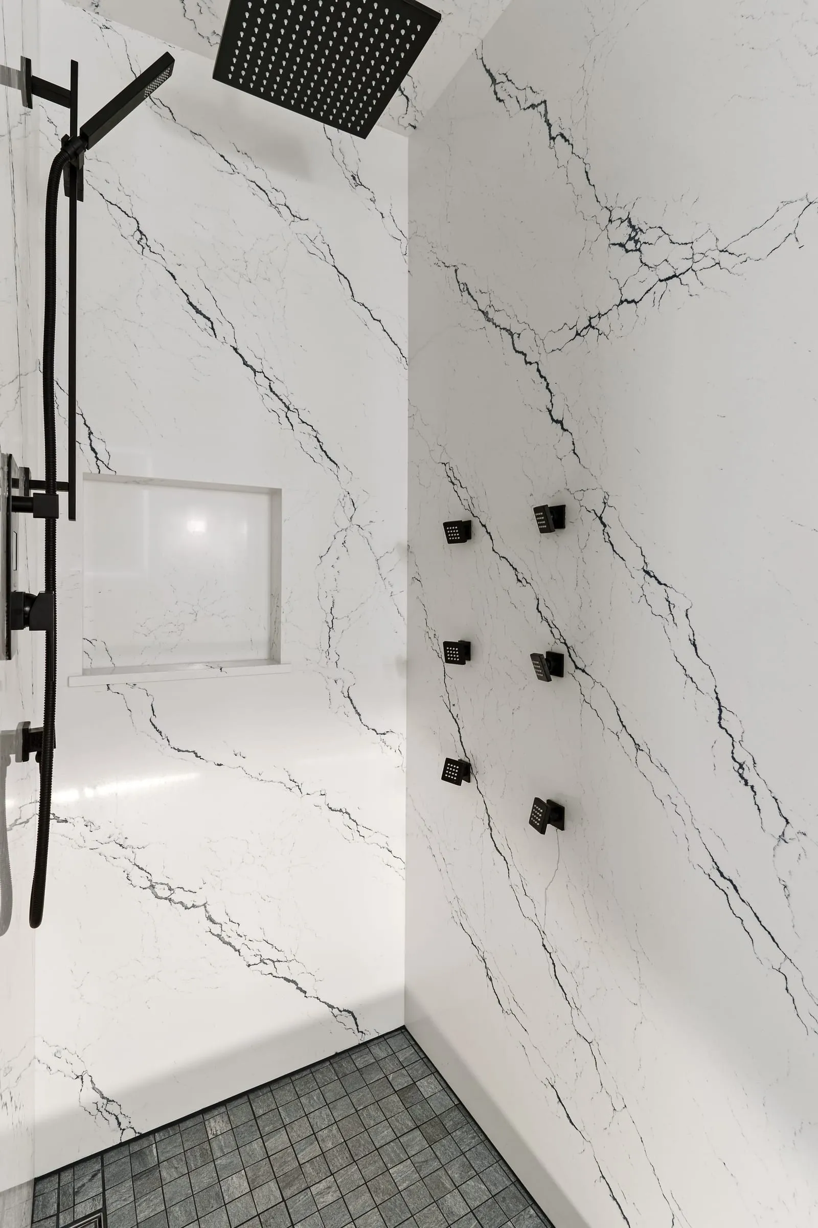 Shower wall in marble-look slab with a matte black shower set and body jets