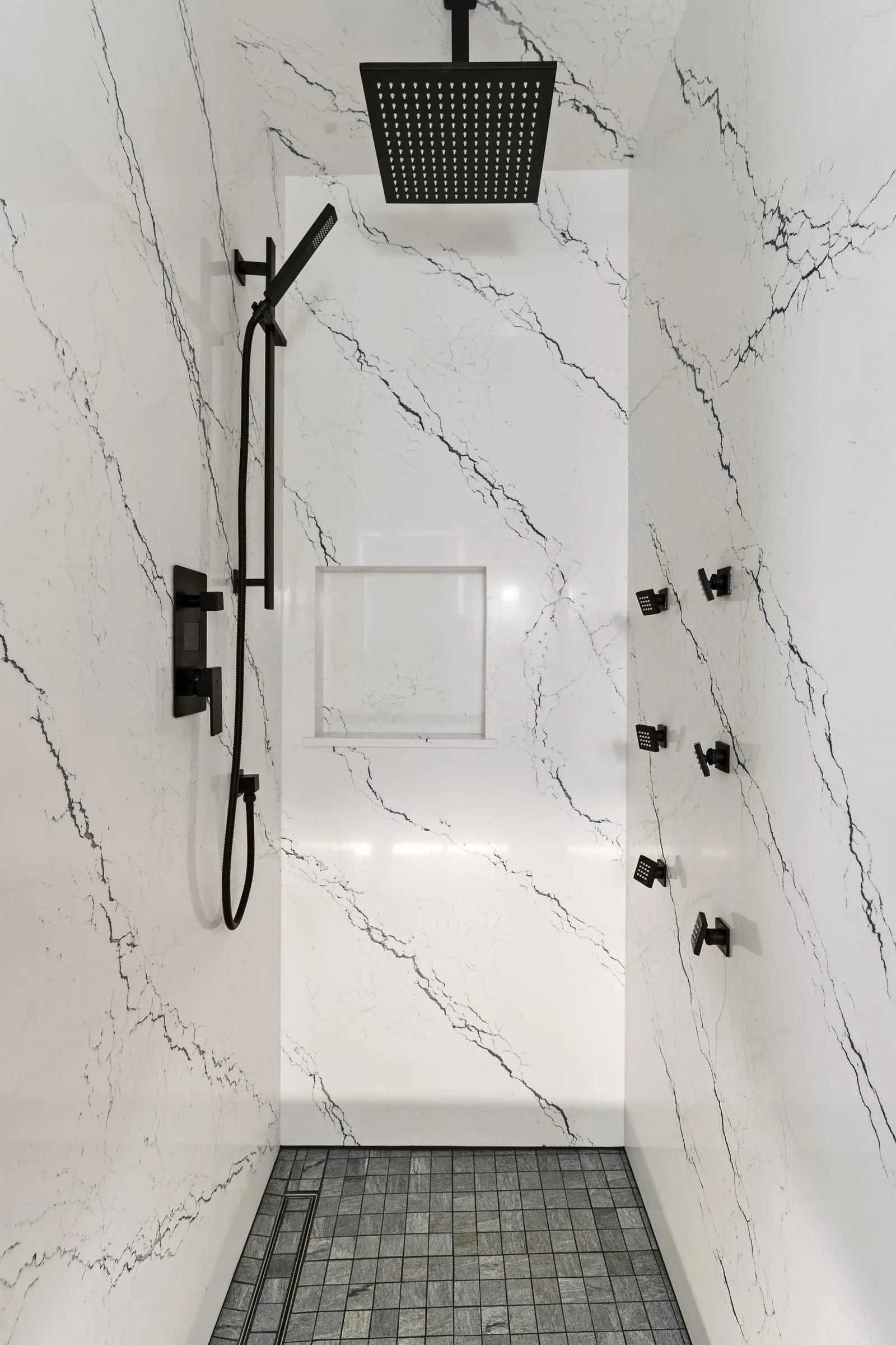 Matte black shower controls and hand shower against the slab wall