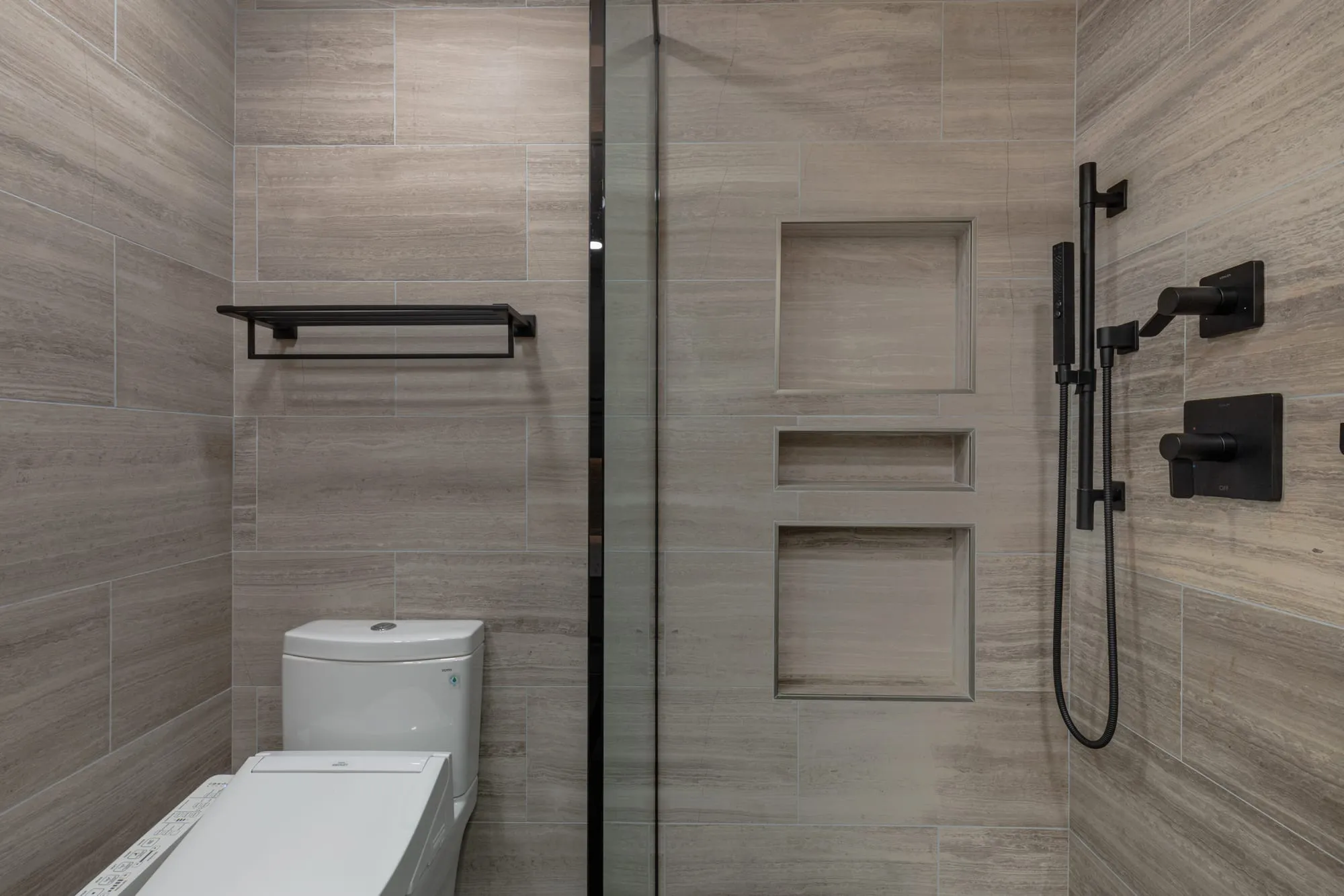 Matte black shower controls and hand shower on a wall bracket beside the recessed niches