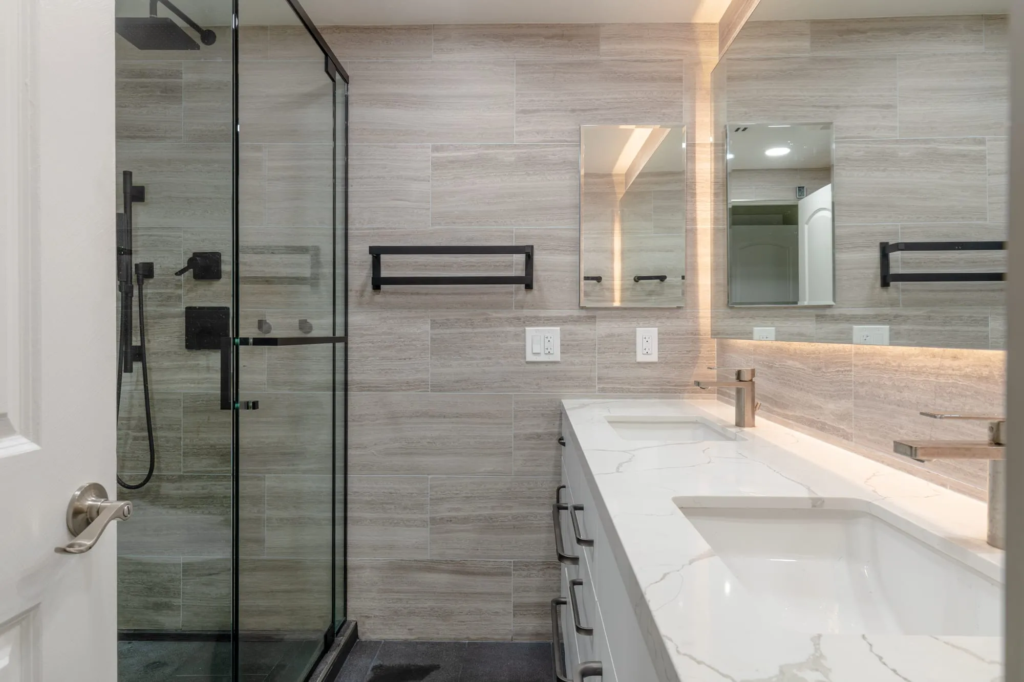 Frameless shower glass with the backlit mirror reflected across the room
