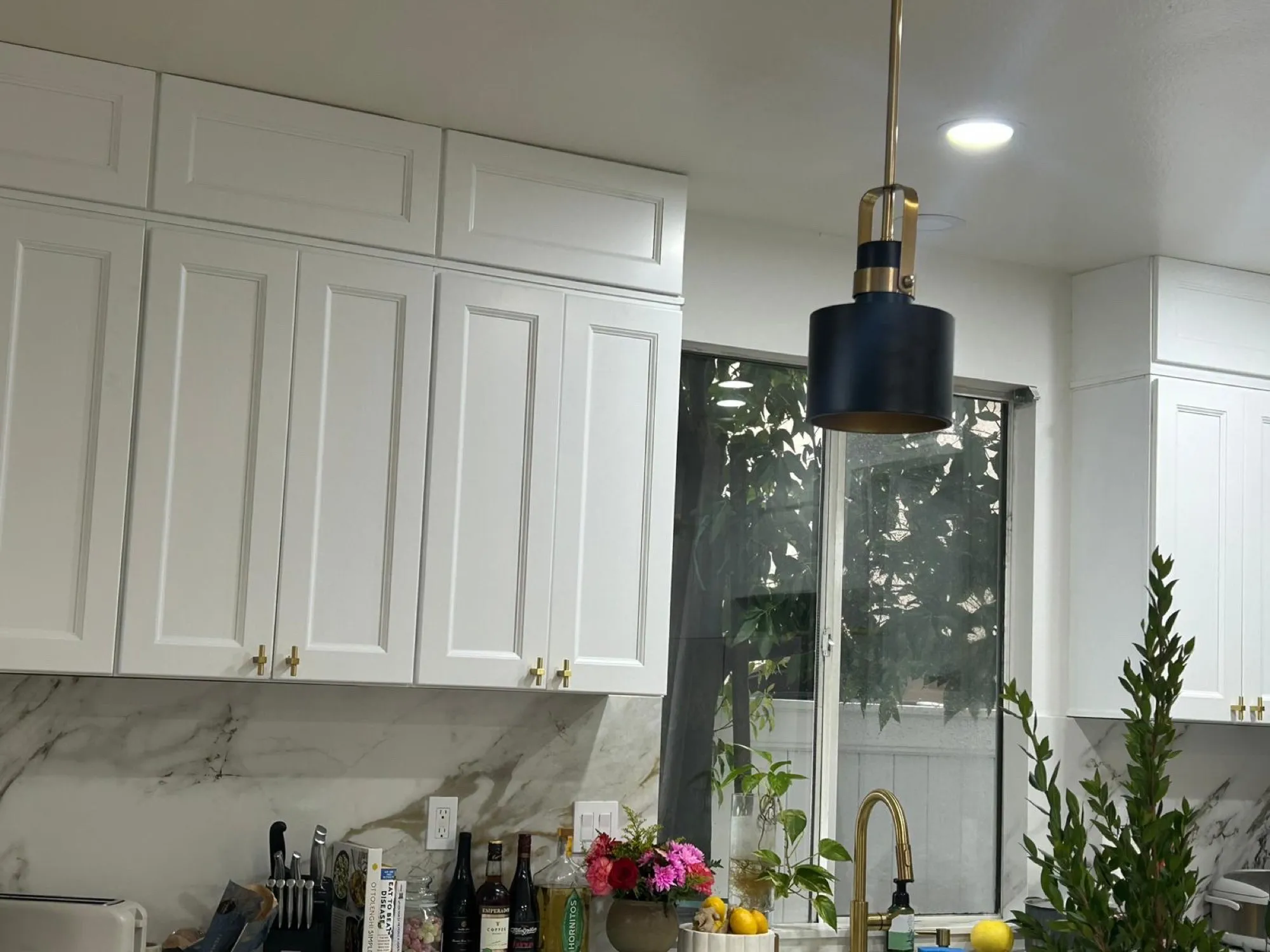Sink under the window with a brushed-gold faucet, pendant above