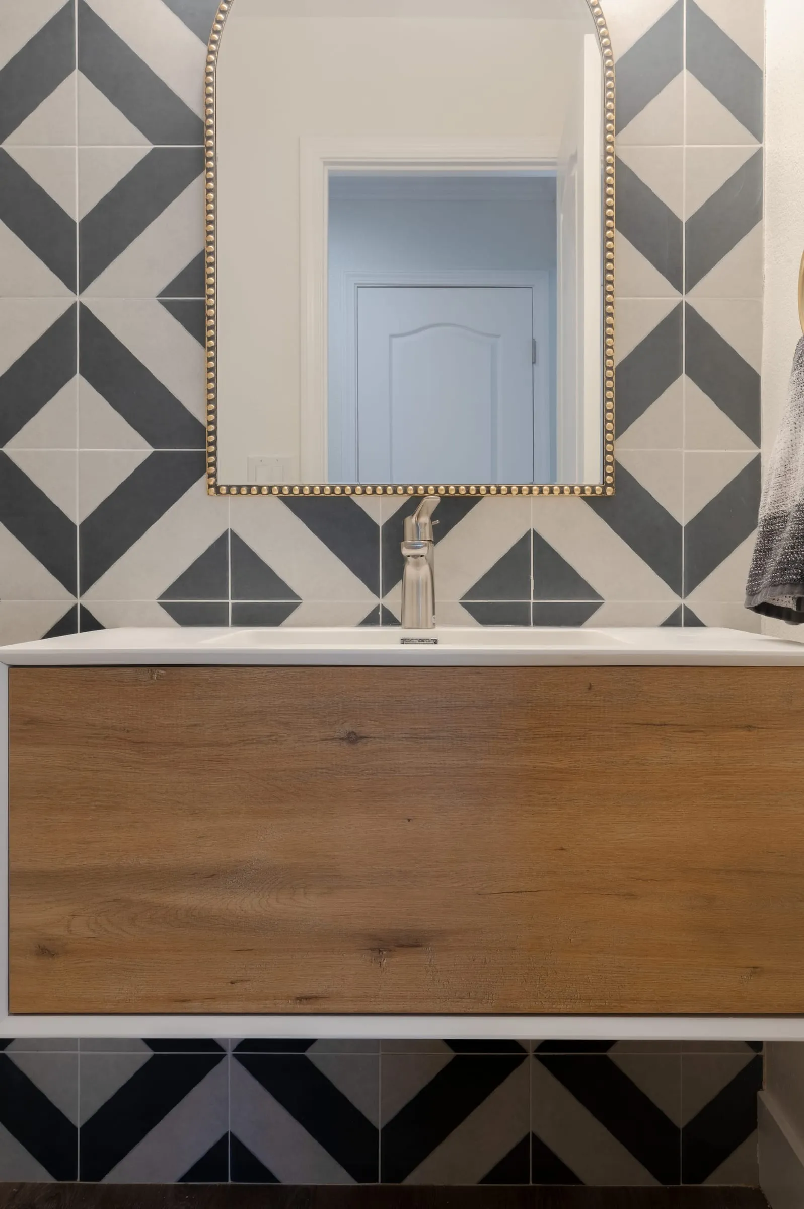 Alcove tub below a gold-framed mirror on the geometric tile wall