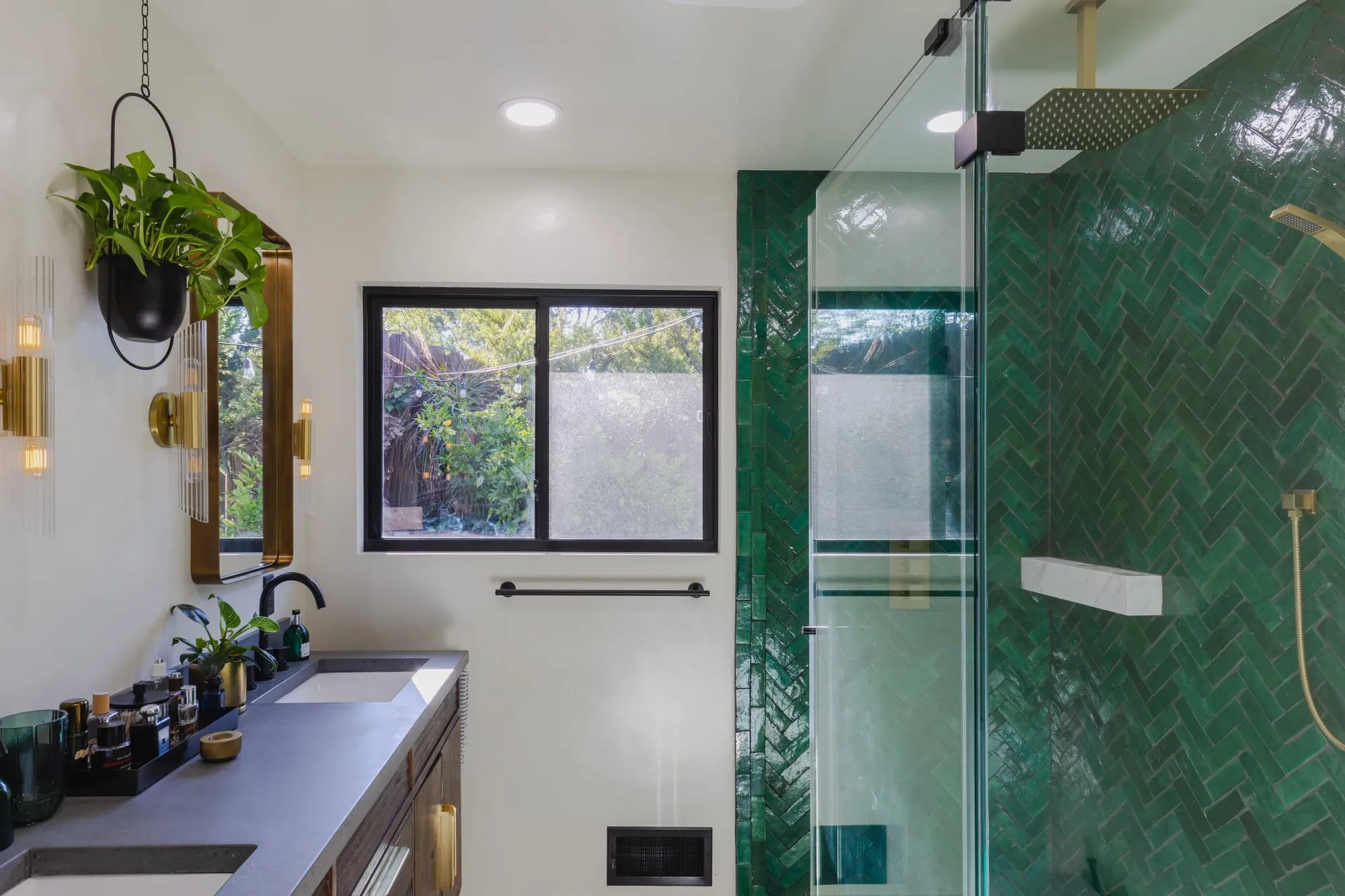 Double vanity with brass-framed mirrors beside the emerald tile shower behind a glass panel