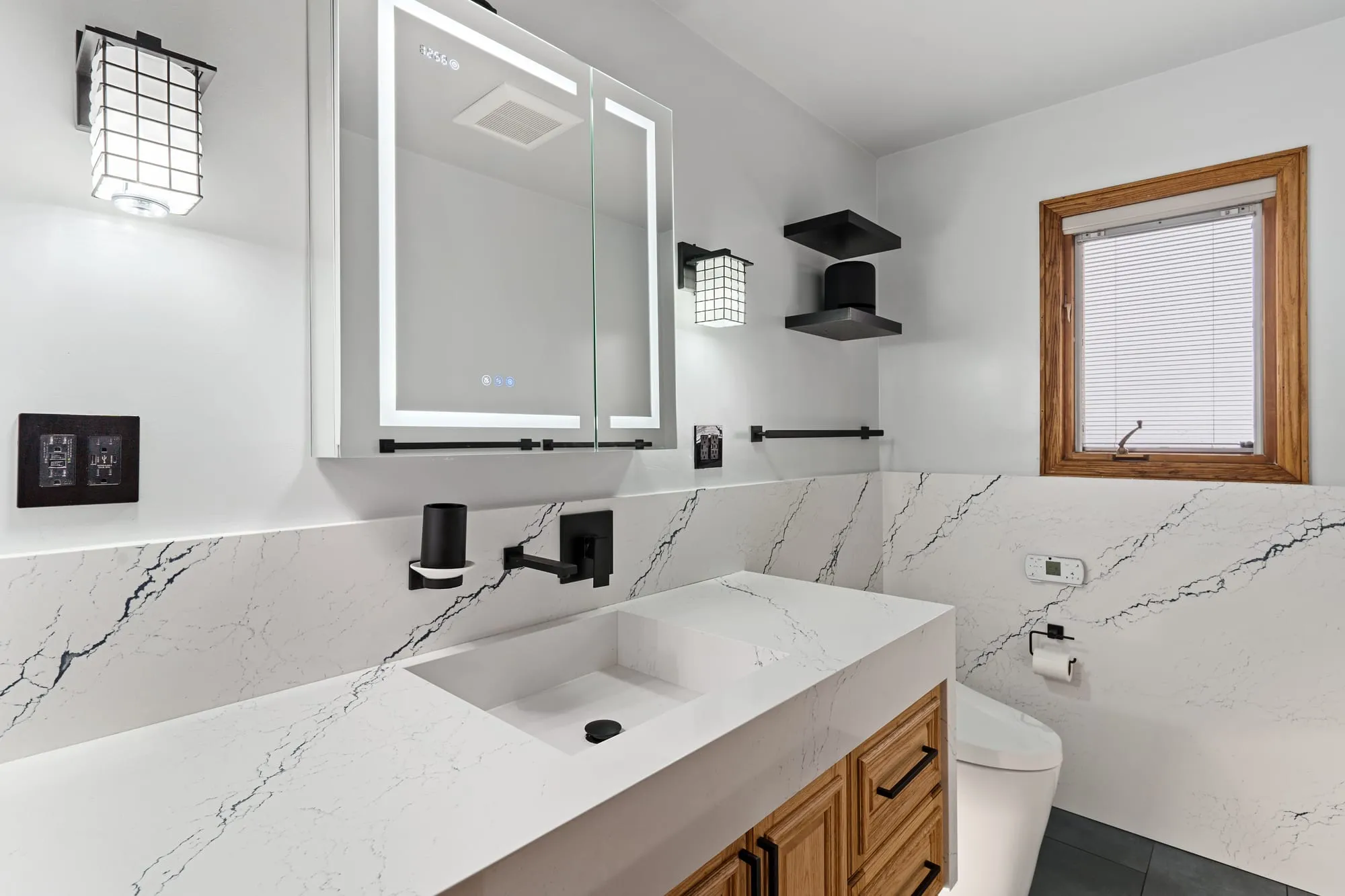 Vanity run under a backlit mirror beside an oak-framed window