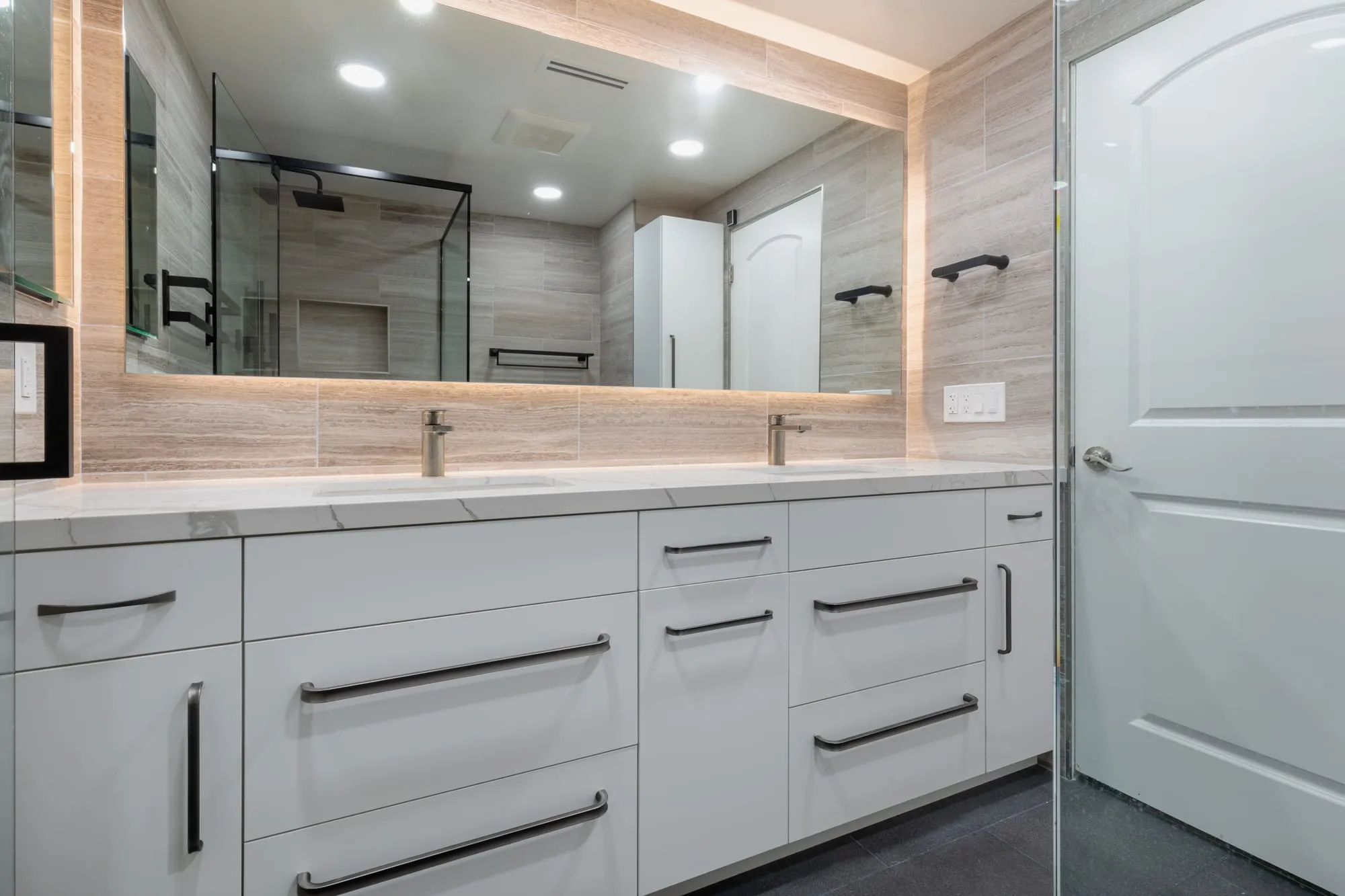 Vanity run beneath a full-width backlit mirror with matte black towel bars either side