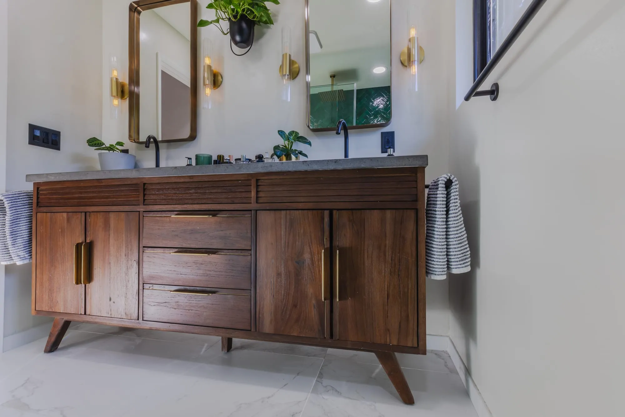 Walnut vanity with tapered legs and brass pulls under a stone counter