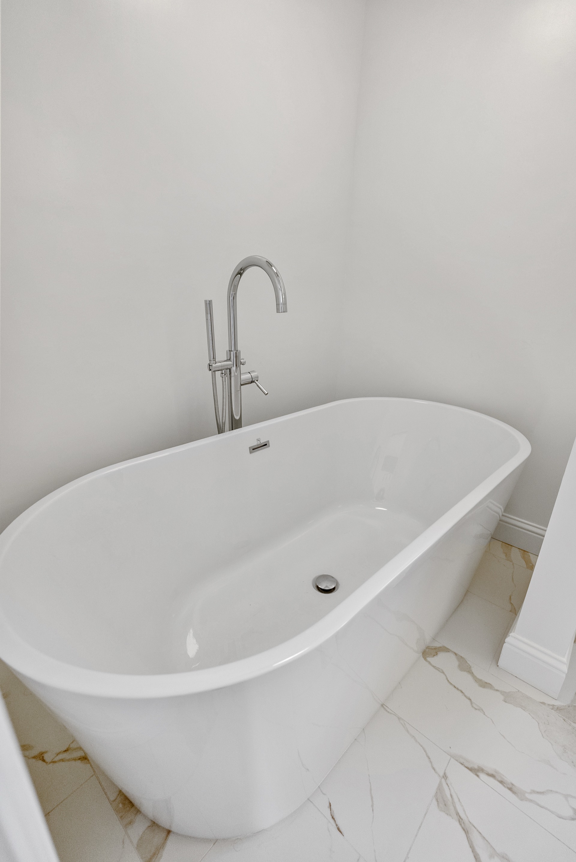 Freestanding white soaking tub with polished nickel floor-mount filler and marble tile