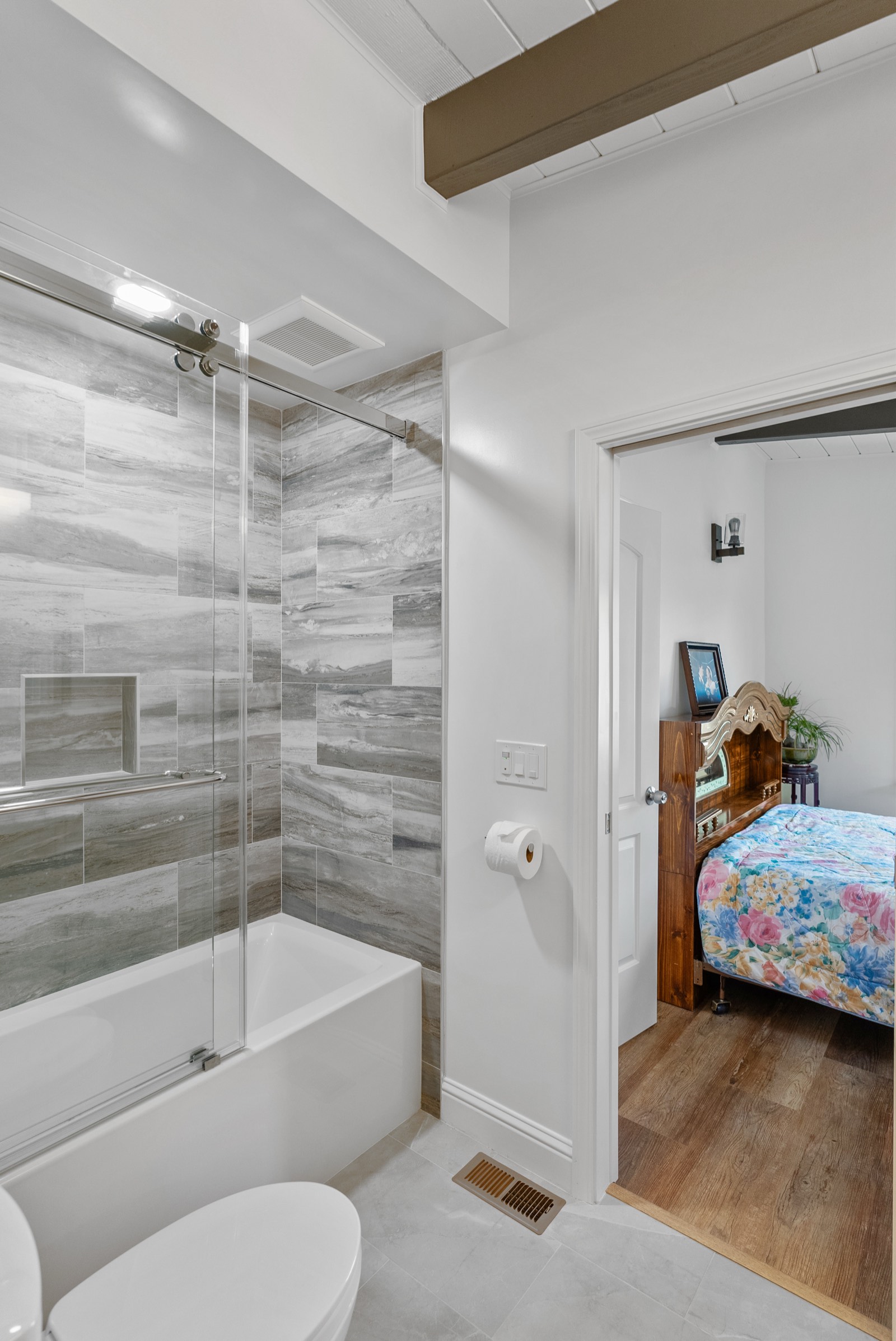Bathroom with marbled gray tile shower/tub surround, glass door, and adjacent bedroom view
