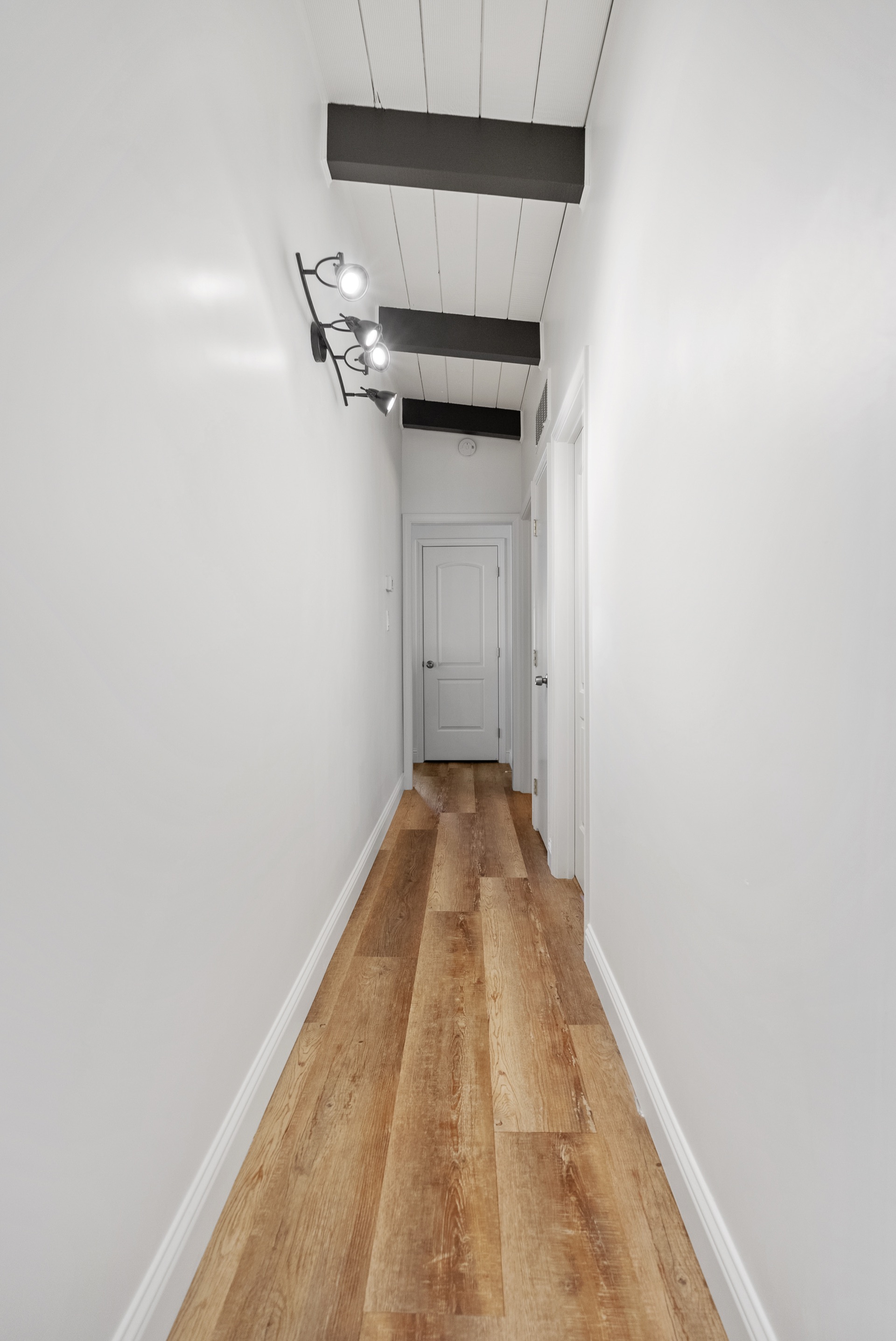 Long hallway with white shiplap ceiling, industrial spotlight sconce, and warm plank floors