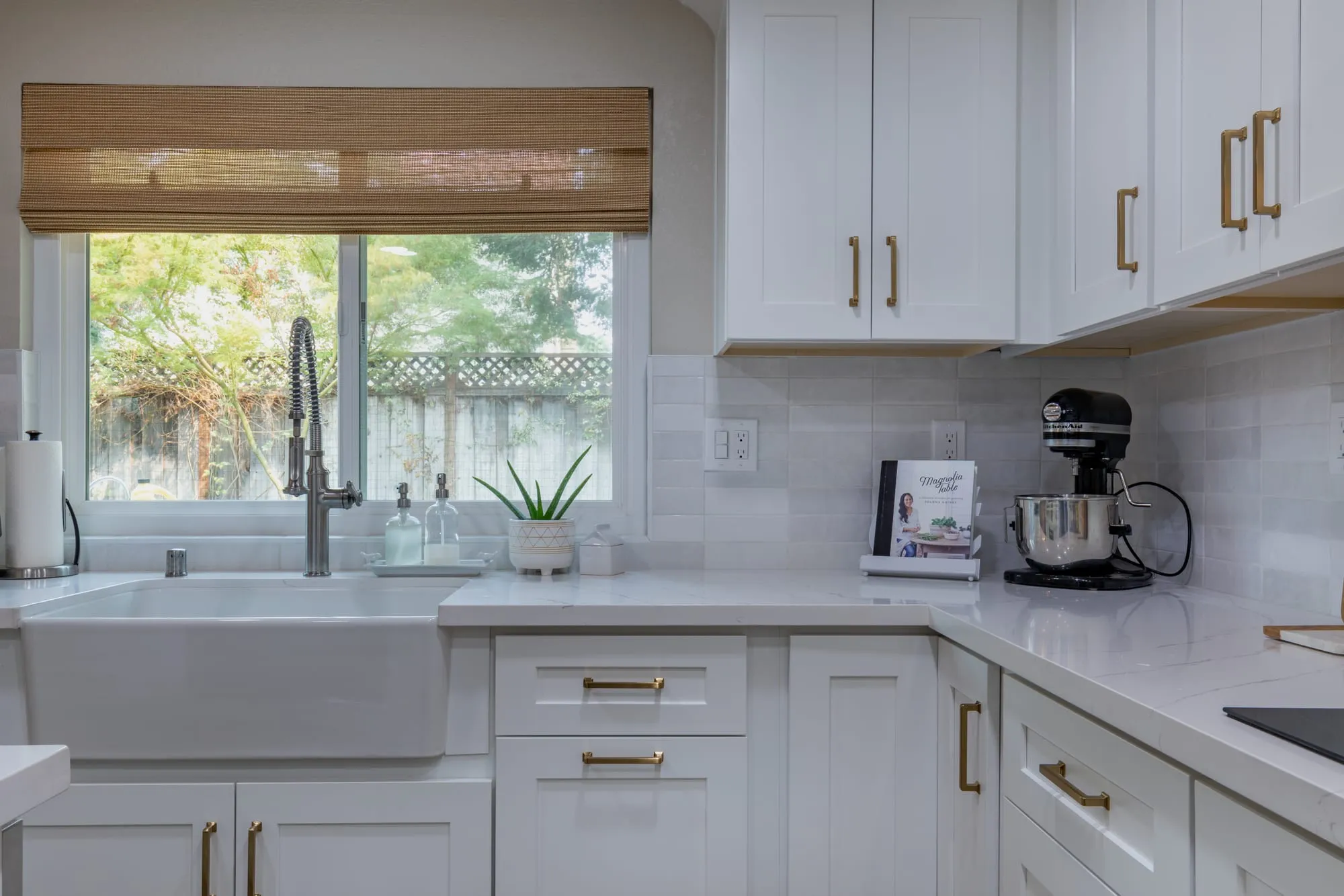 Window run of white shaker cabinetry with brass pulls and a quartz counter
